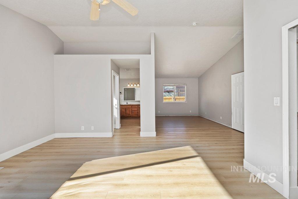 Unfurnished bedroom featuring light wood-style flooring, ensuite bath, ceiling fan, and lofted ceiling