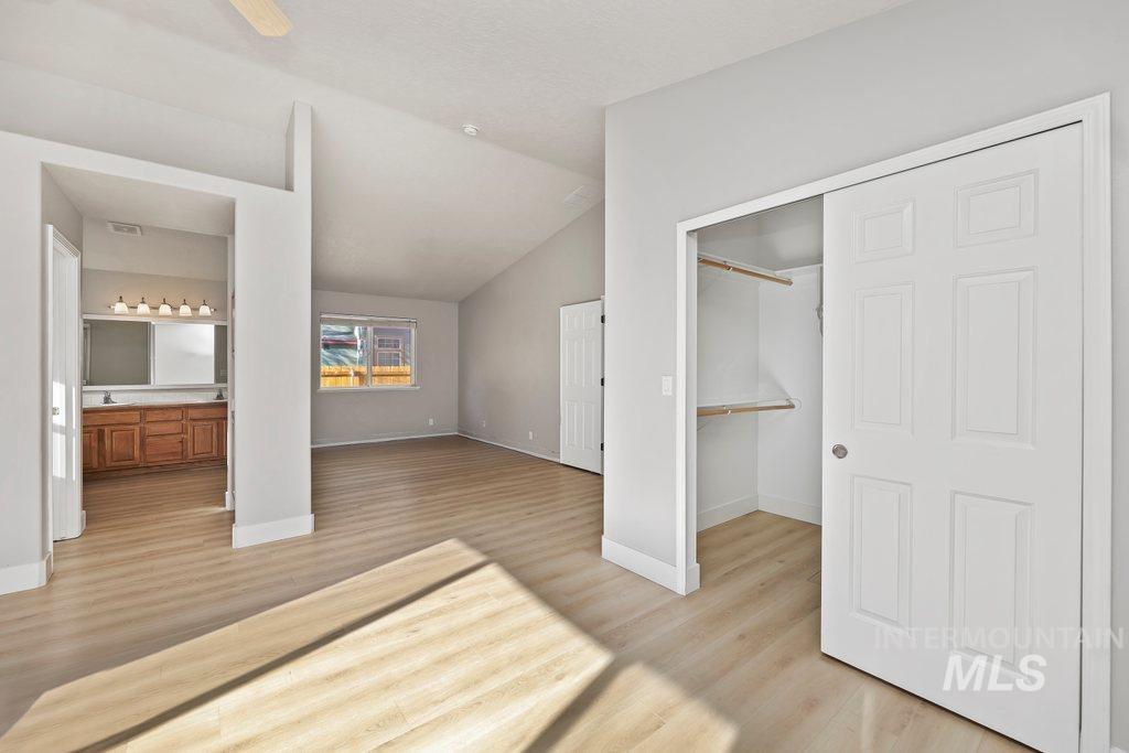 Unfurnished bedroom with a closet, light wood-style flooring, lofted ceiling, ceiling fan, and ensuite bath