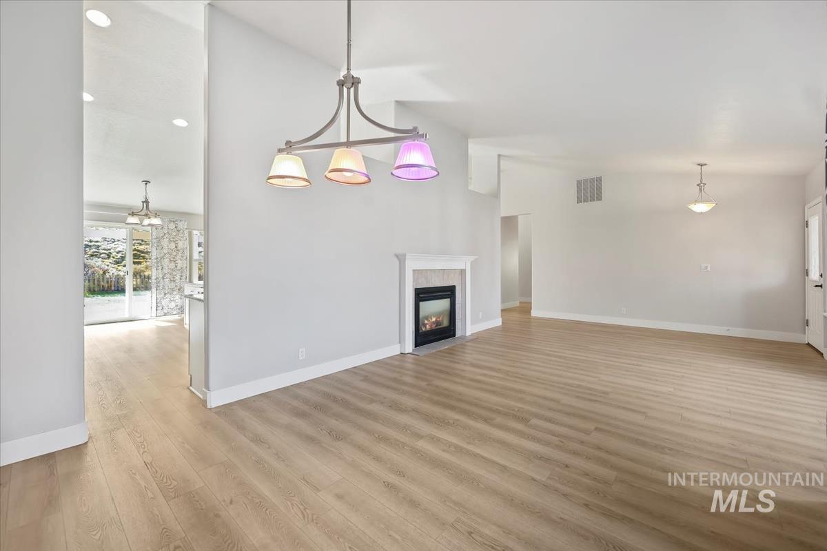 Unfurnished living room with light wood-type flooring, a fireplace, high vaulted ceiling, a chandelier, and recessed lighting