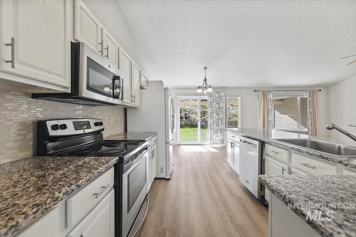Kitchen with stainless steel appliances, white cabinets, light wood-style flooring, decorative backsplash, and dark stone counters