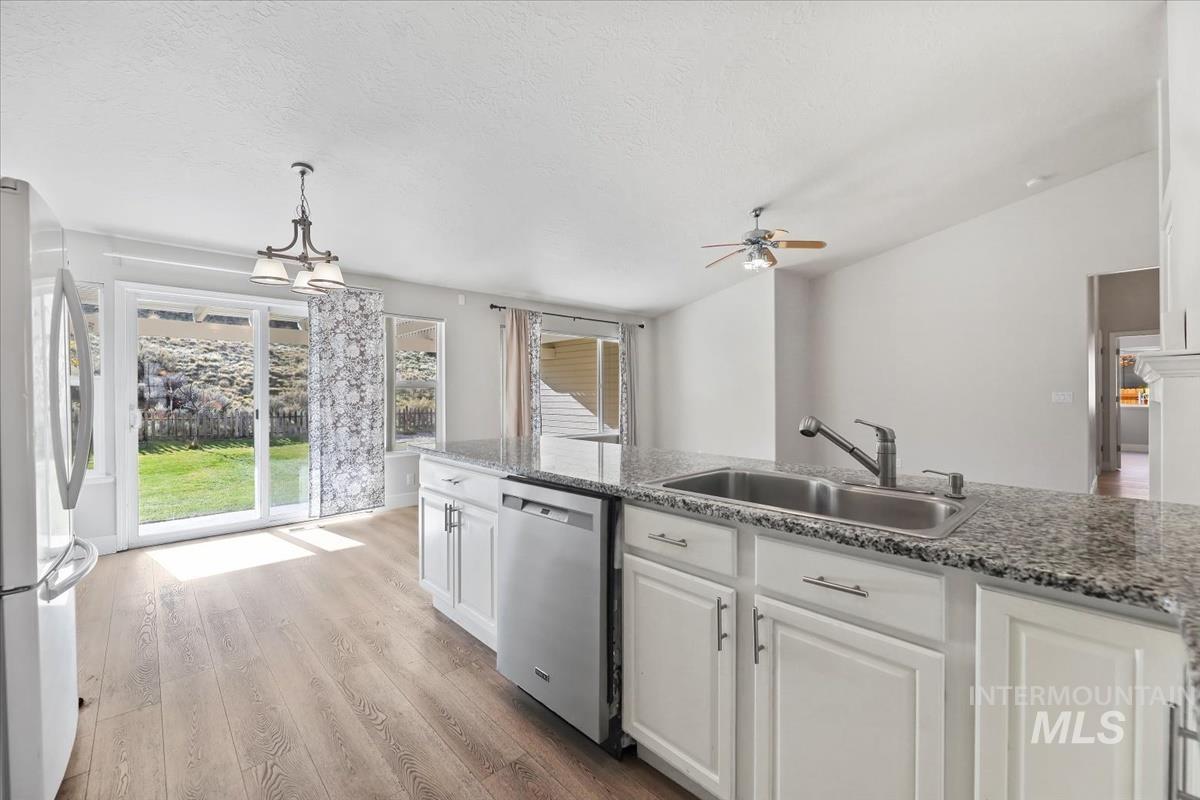 Kitchen featuring white cabinets, light wood-type flooring, freestanding refrigerator, stainless steel dishwasher, and decorative light fixtures