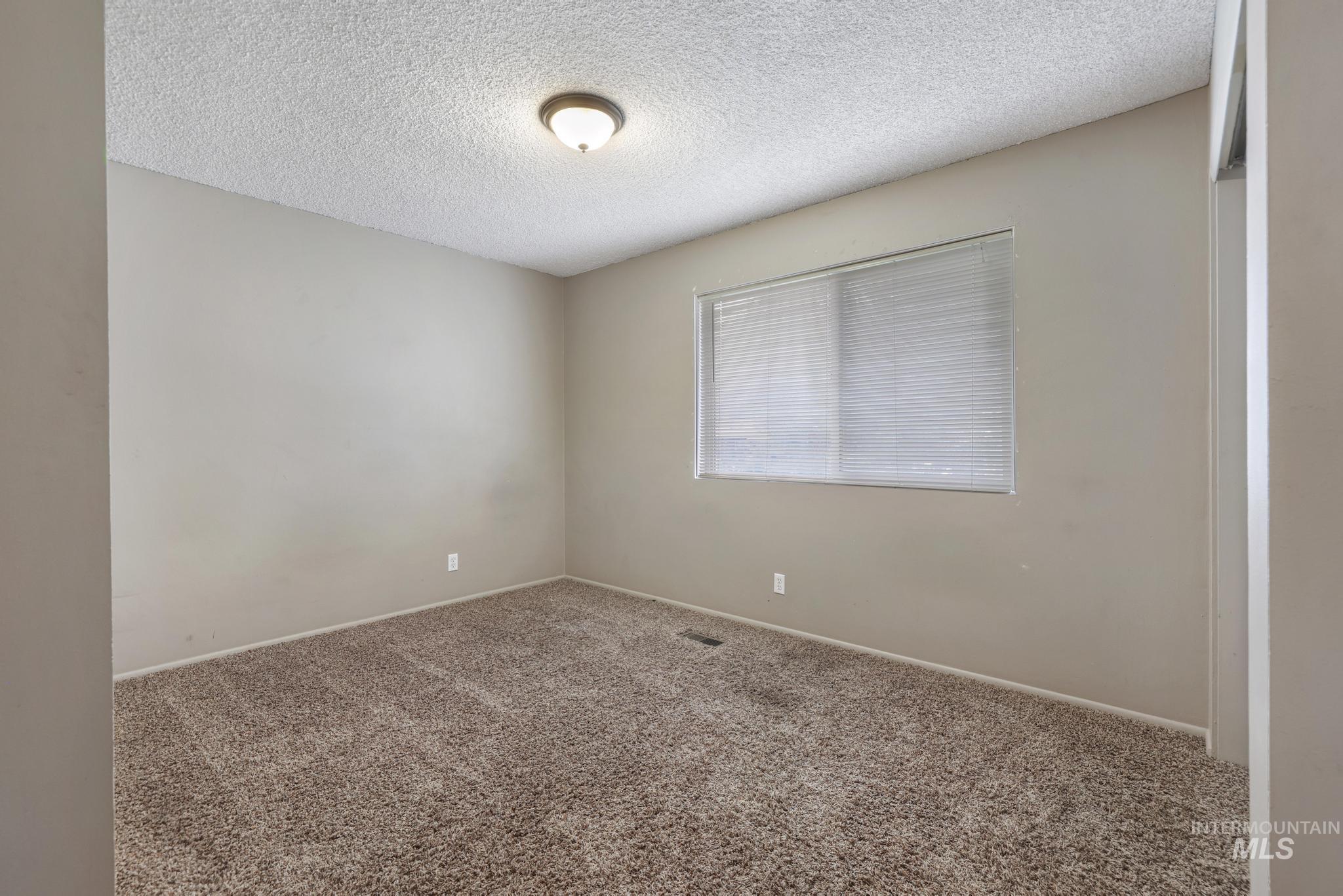 Carpeted empty room with a textured ceiling and baseboards