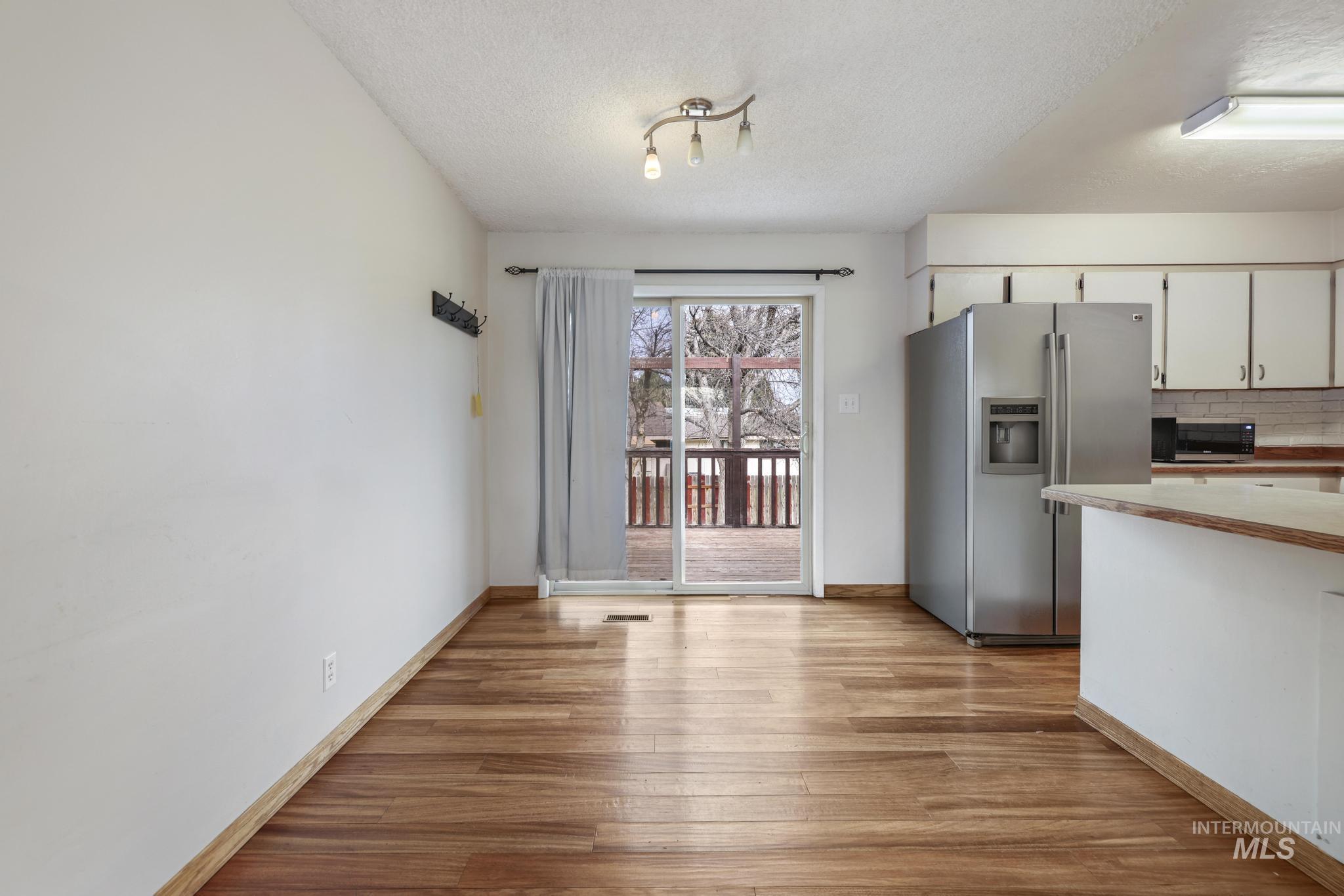 Kitchen featuring appliances with stainless steel finishes, light wood-style flooring, a textured ceiling, decorative backsplash, and white cabinetry