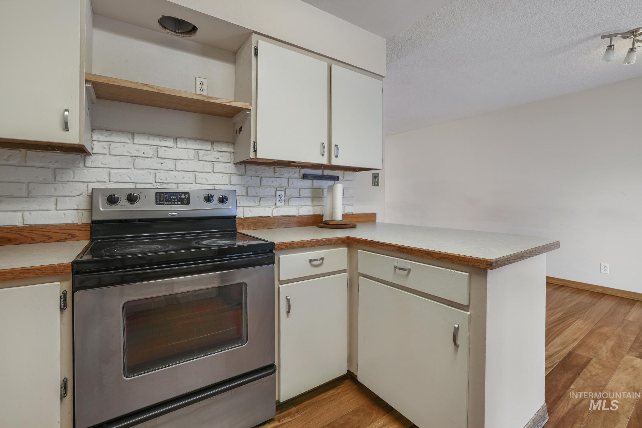 Kitchen with stainless steel range with electric cooktop, open shelves, a peninsula, light countertops, and decorative backsplash