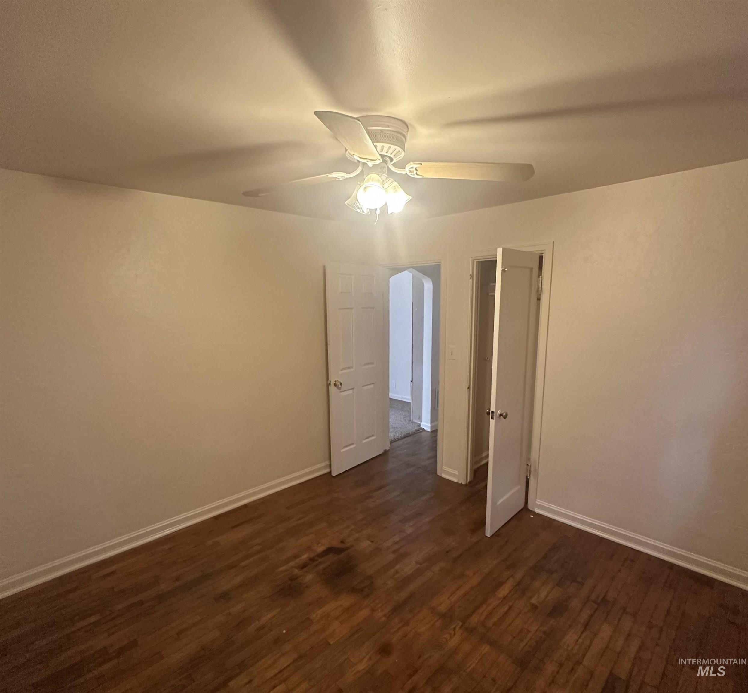 Empty room with dark wood-style flooring and a ceiling fan