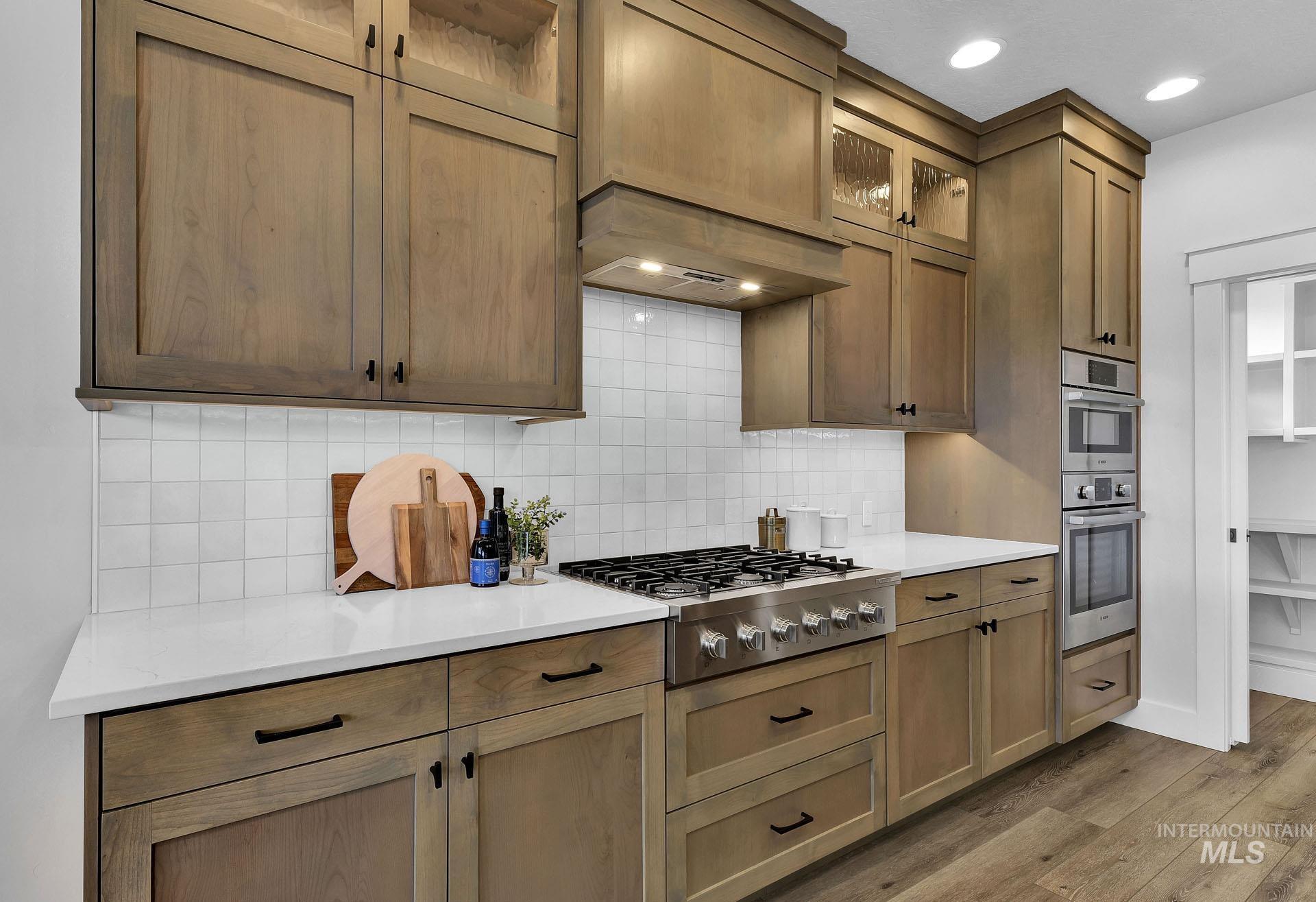 Kitchen featuring glass insert cabinets, stainless steel appliances, light wood-style floors, custom exhaust hood, and light stone countertops