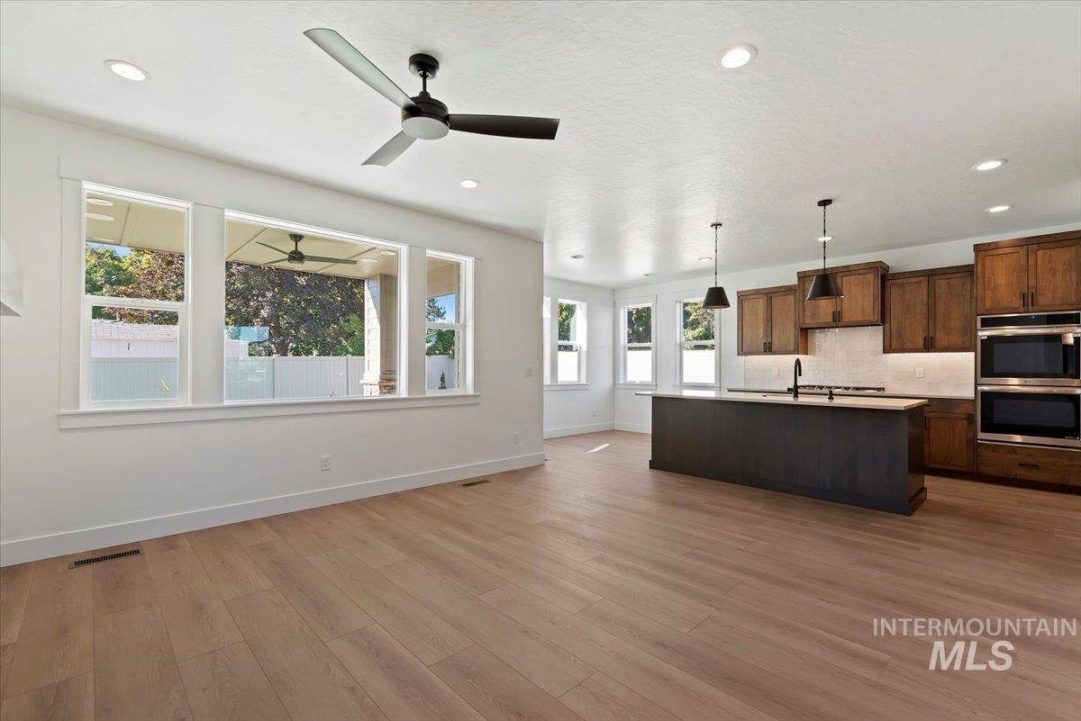 Kitchen featuring stainless steel double oven, pendant lighting, open floor plan, decorative backsplash, and light wood finished floors