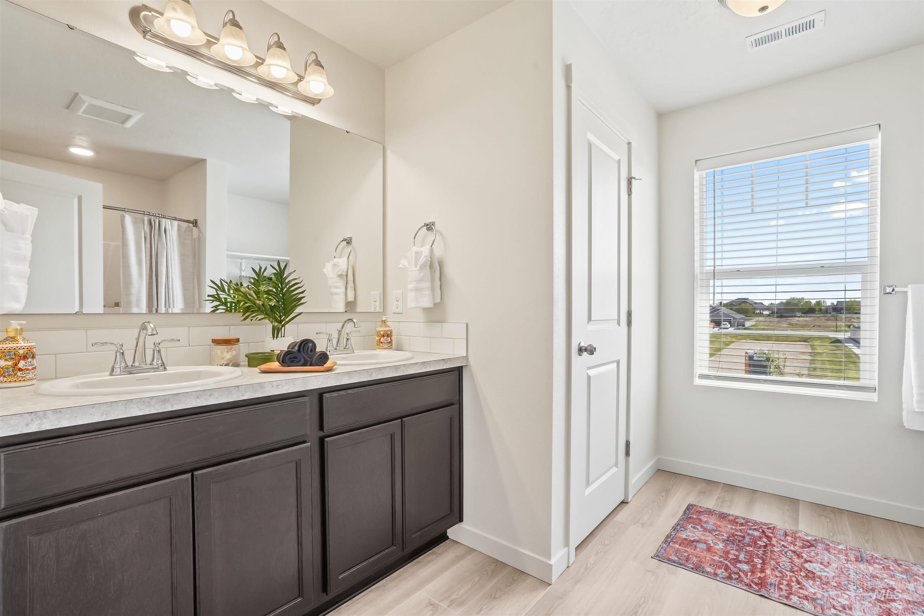 Bathroom featuring double vanity, a shower with shower curtain, and light wood-style floors