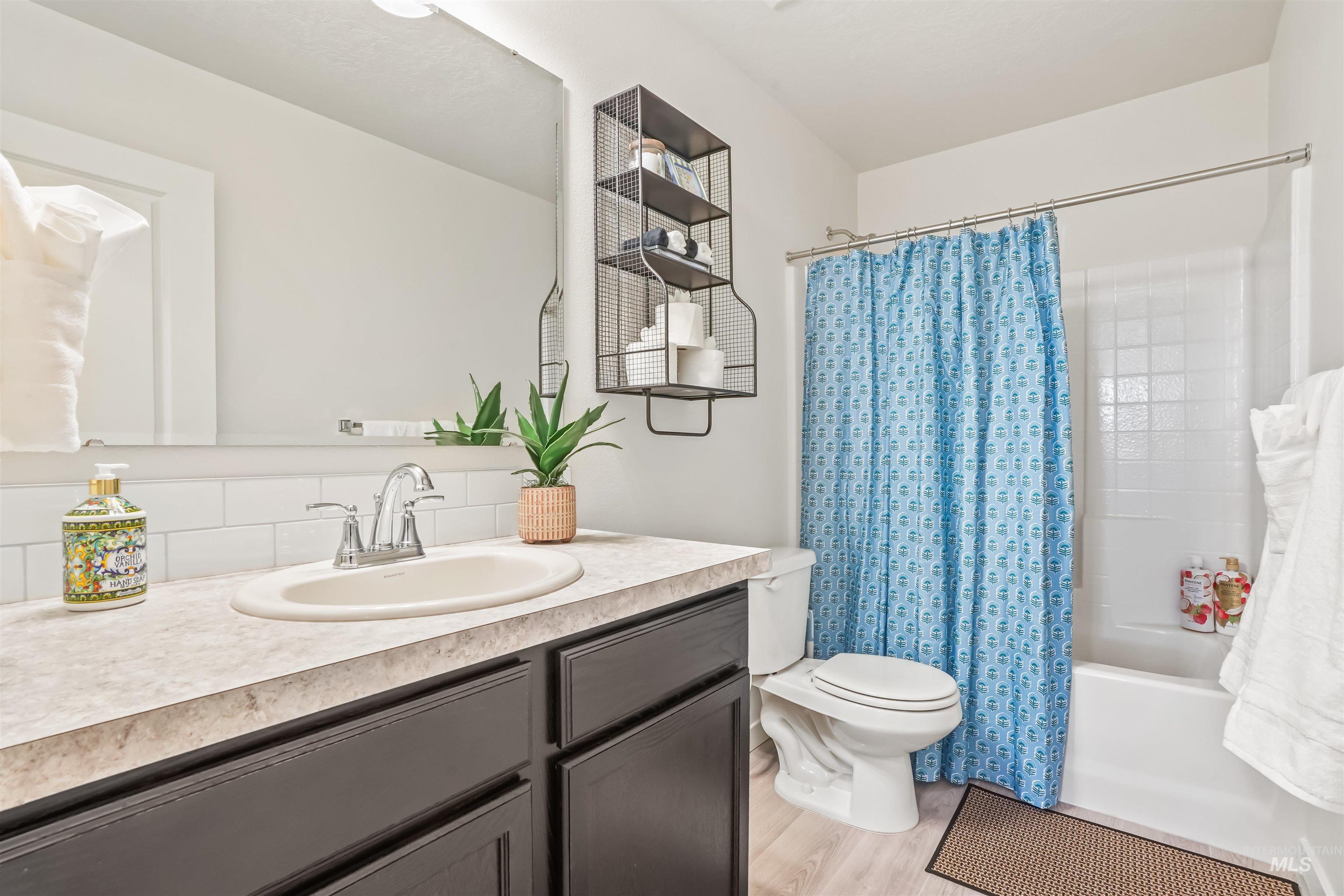 Bathroom featuring shower / bathtub combination with curtain, vanity, light wood-style flooring, and tasteful backsplash