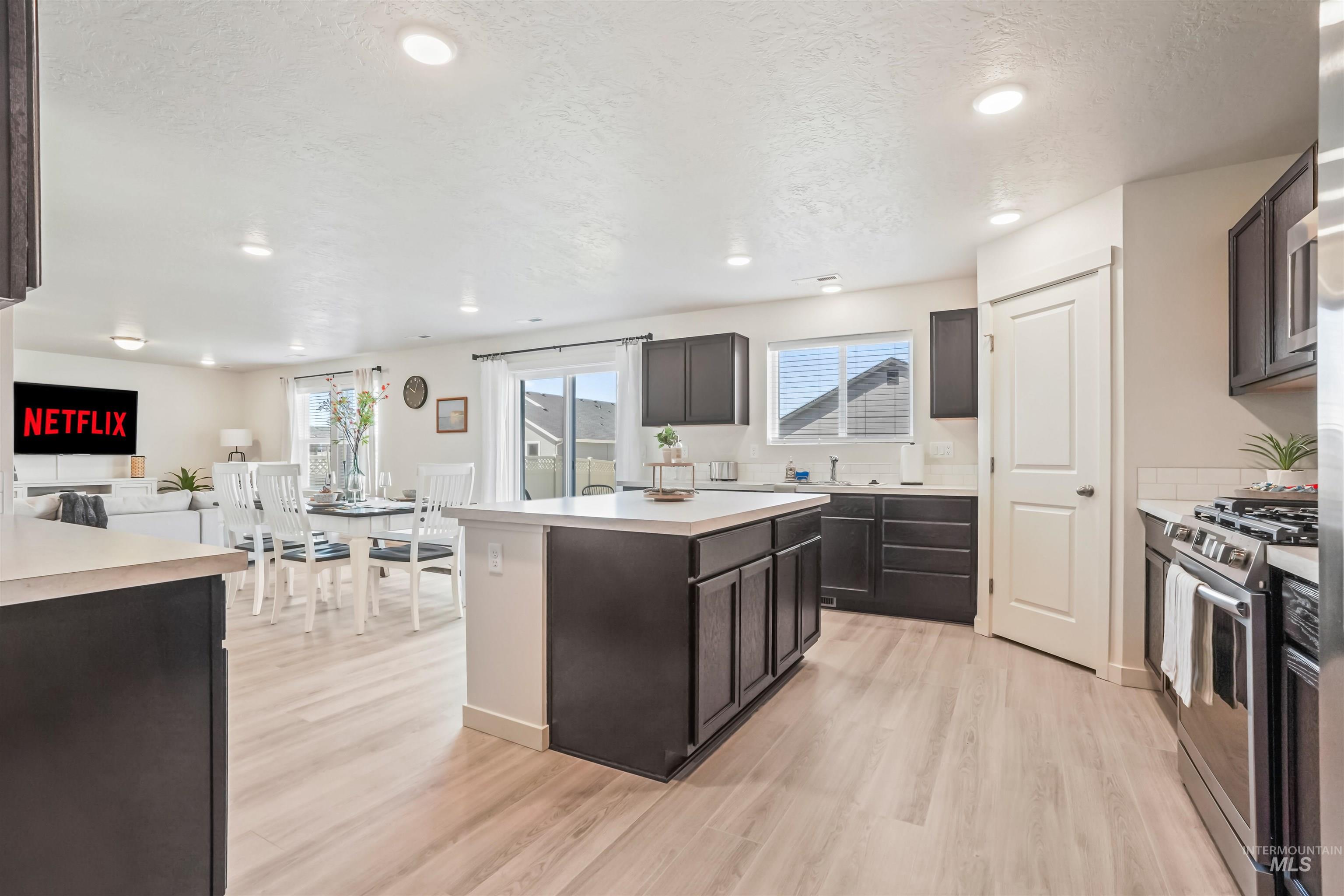 Kitchen with stainless steel gas range, light wood-type flooring, a center island, dark brown cabinetry, and recessed lighting