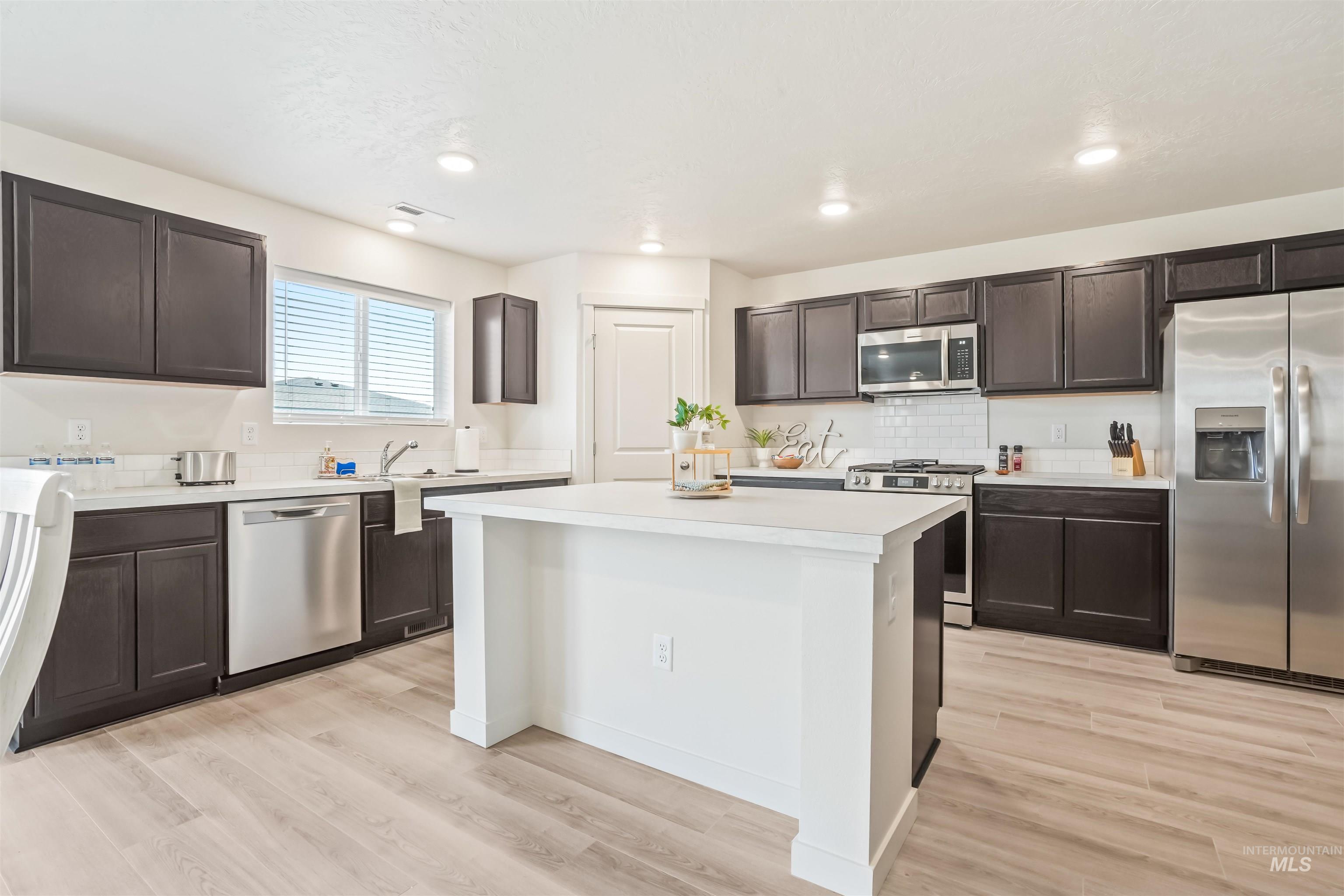 Kitchen with stainless steel appliances, light countertops, light wood-style flooring, tasteful backsplash, and dark brown cabinets