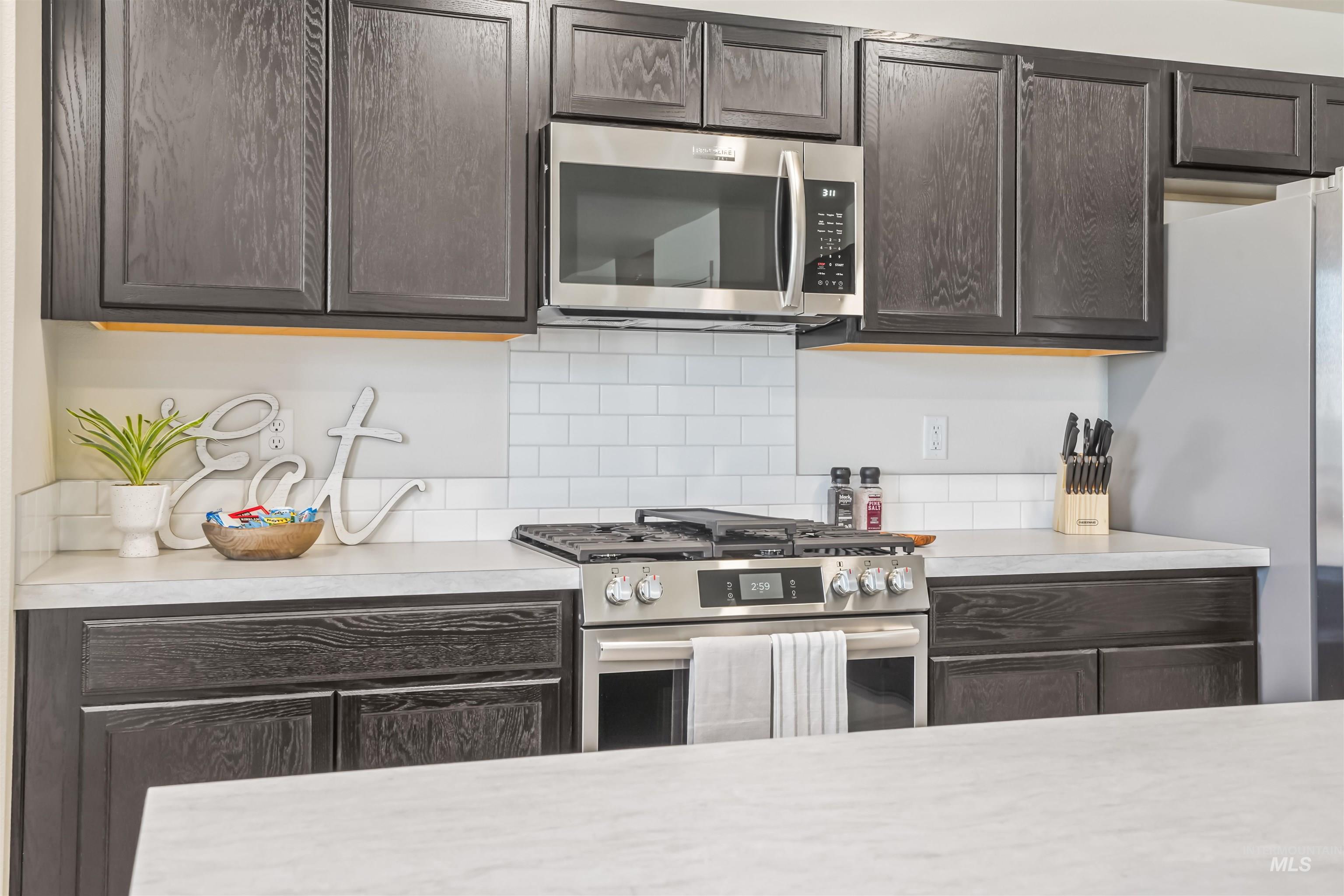 Kitchen with stainless steel appliances, light countertops, dark brown cabinets, and decorative backsplash