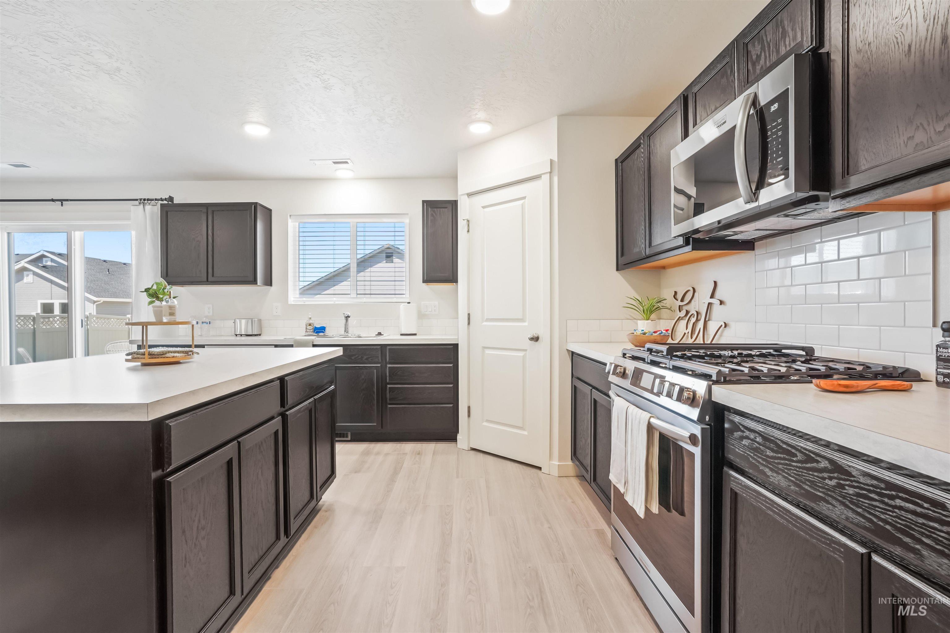 Kitchen featuring appliances with stainless steel finishes, light countertops, dark brown cabinets, light wood-type flooring, and decorative backsplash