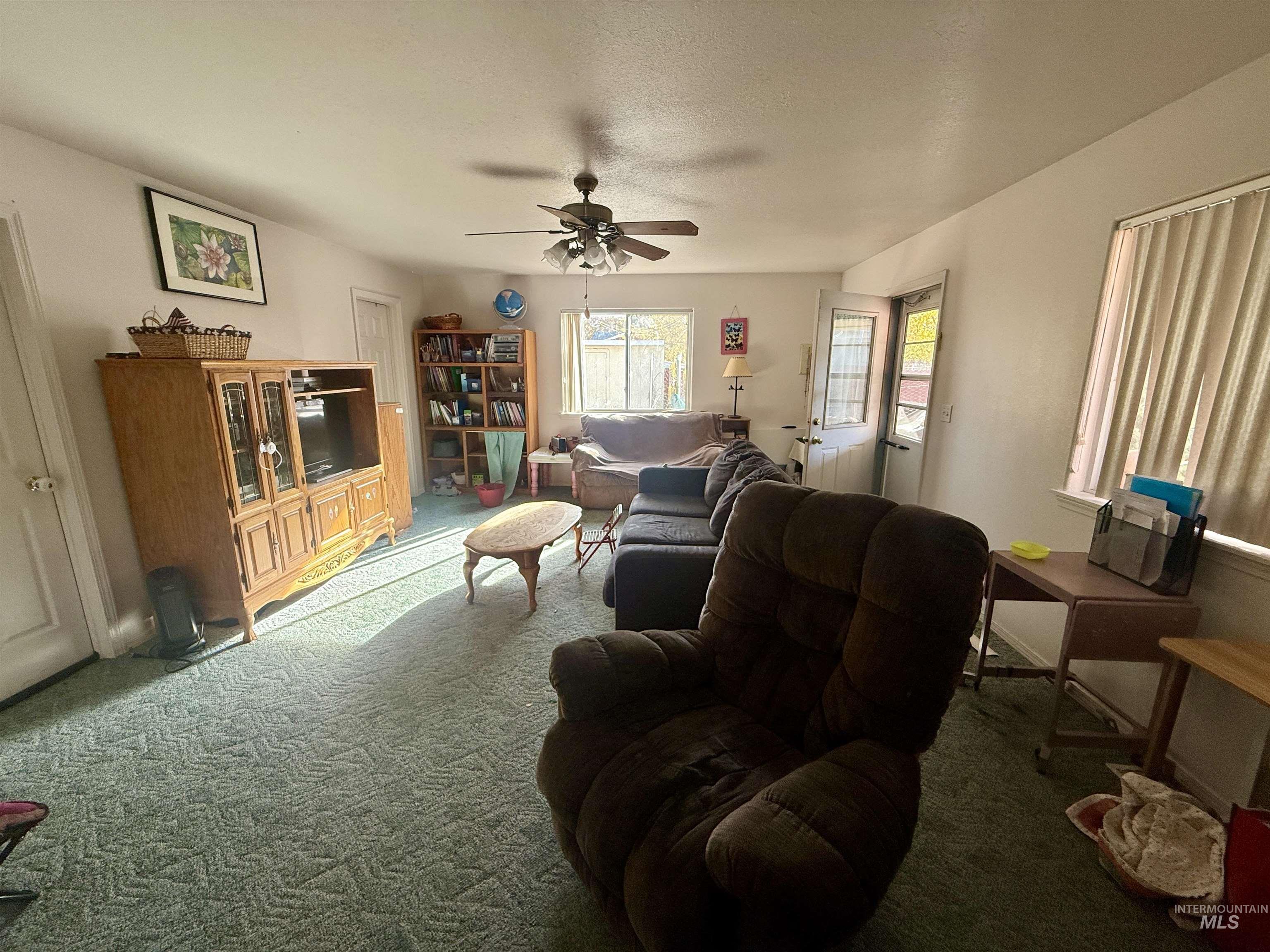 Carpeted living room featuring ceiling fan and a textured ceiling