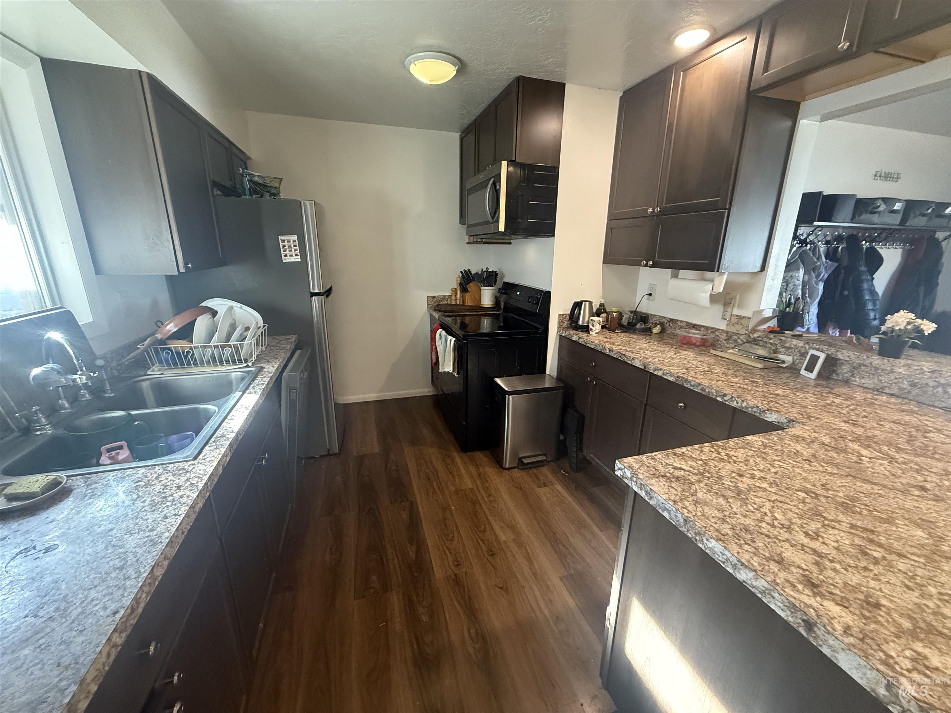 Kitchen featuring dark wood-style flooring, electric range, stainless steel microwave, dark brown cabinetry, and light stone countertops