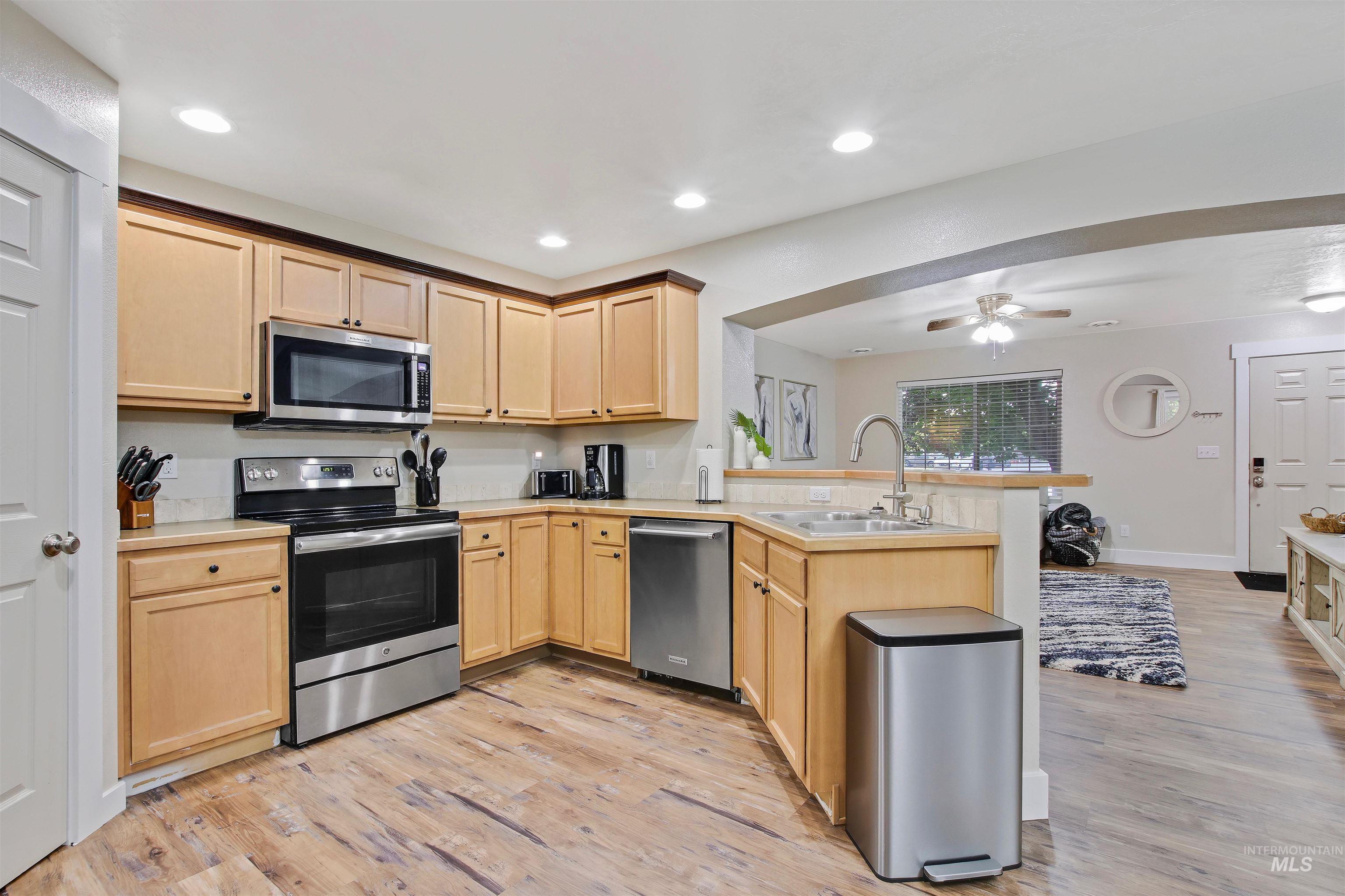 Kitchen with appliances with stainless steel finishes, a peninsula, light brown cabinets, light wood-type flooring, and recessed lighting