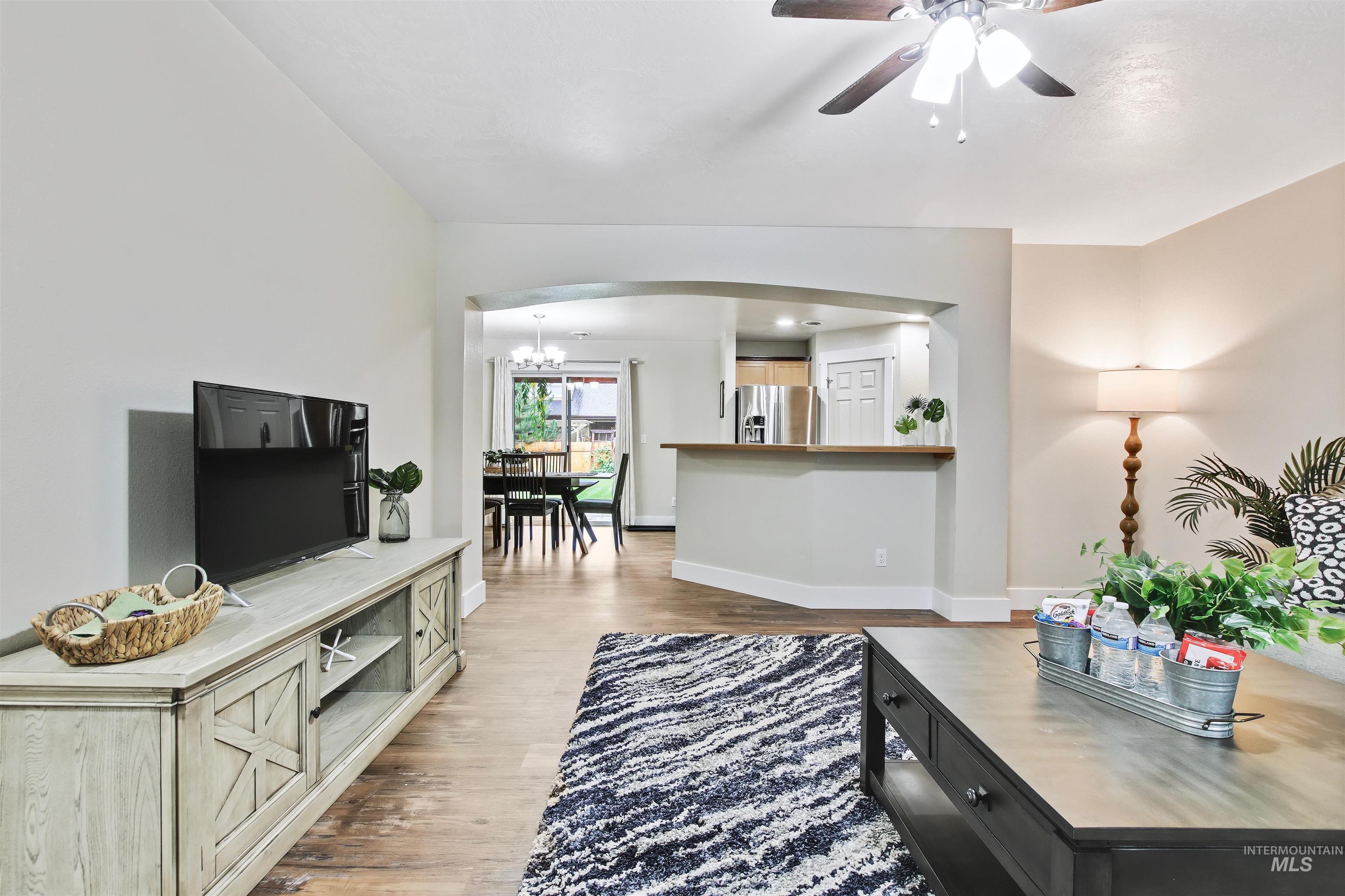 Living room with light wood-style flooring, a ceiling fan, arched walkways, and a chandelier