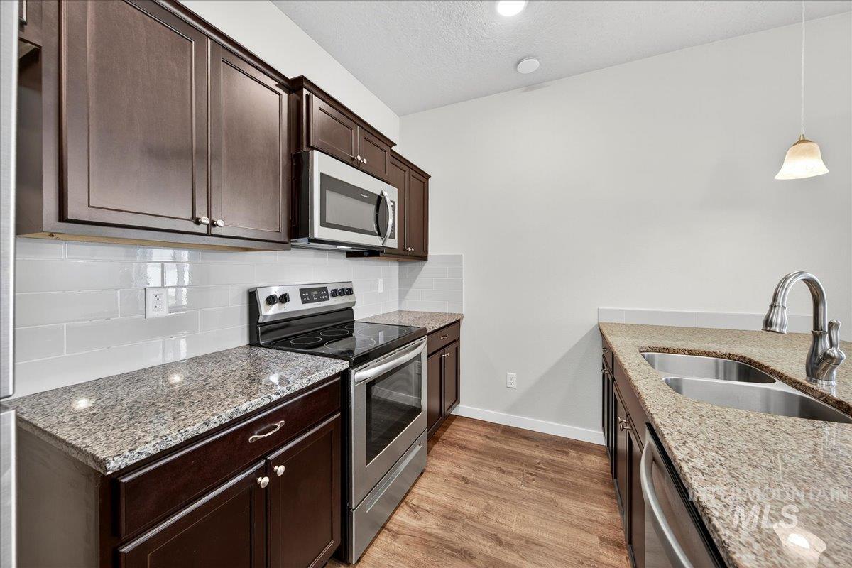 Kitchen with stainless steel appliances, light stone countertops, light wood-style flooring, hanging light fixtures, and dark brown cabinetry