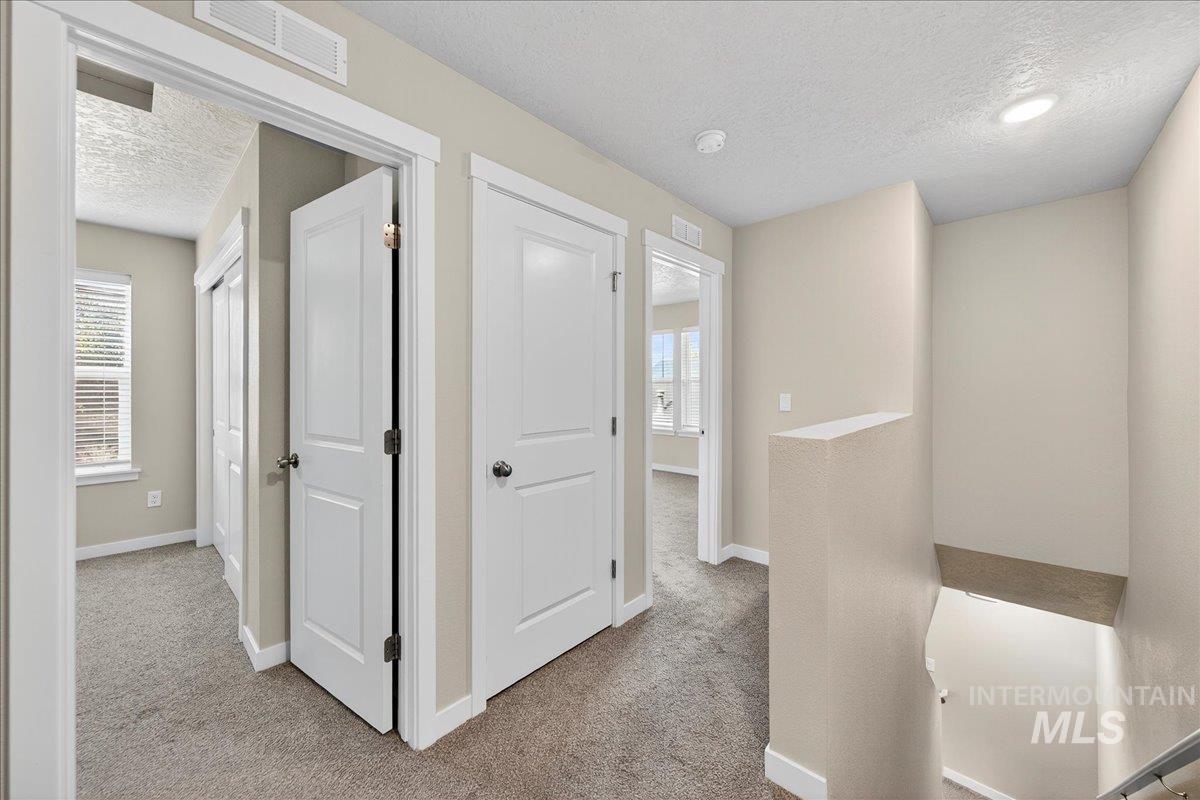 Corridor featuring a textured ceiling, light carpet, an upstairs landing, and healthy amount of natural light