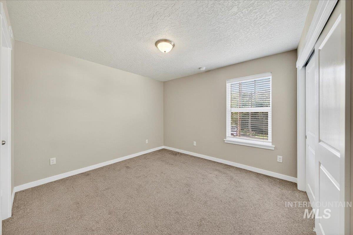 Unfurnished bedroom with a textured ceiling, light carpet, and a closet