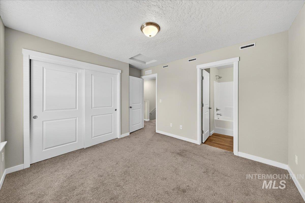 Unfurnished bedroom with a textured ceiling, light colored carpet, a closet, and ensuite bathroom