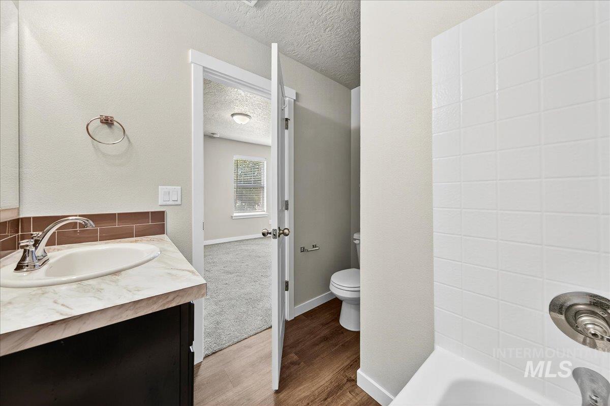 Full bath featuring vanity, a textured ceiling, wood finished floors, and shower / bathtub combination