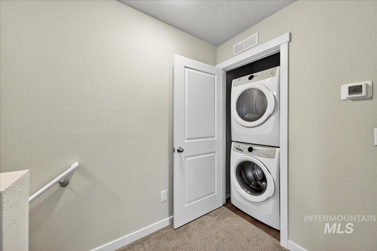 Laundry room featuring estacked washer and dryer, light carpet, and a textured ceiling