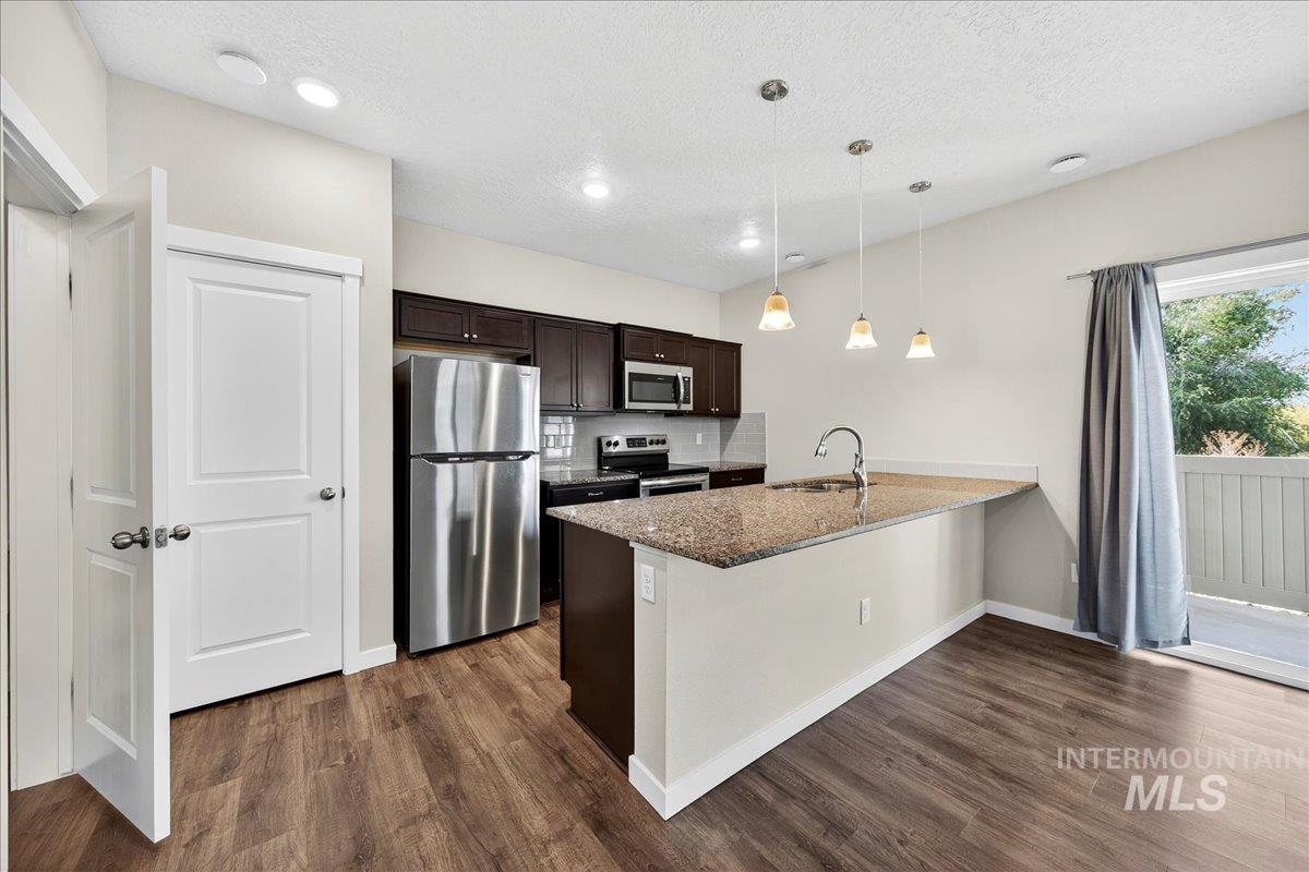Kitchen with dark brown cabinets, appliances with stainless steel finishes, a peninsula, light stone counters, and hanging light fixtures