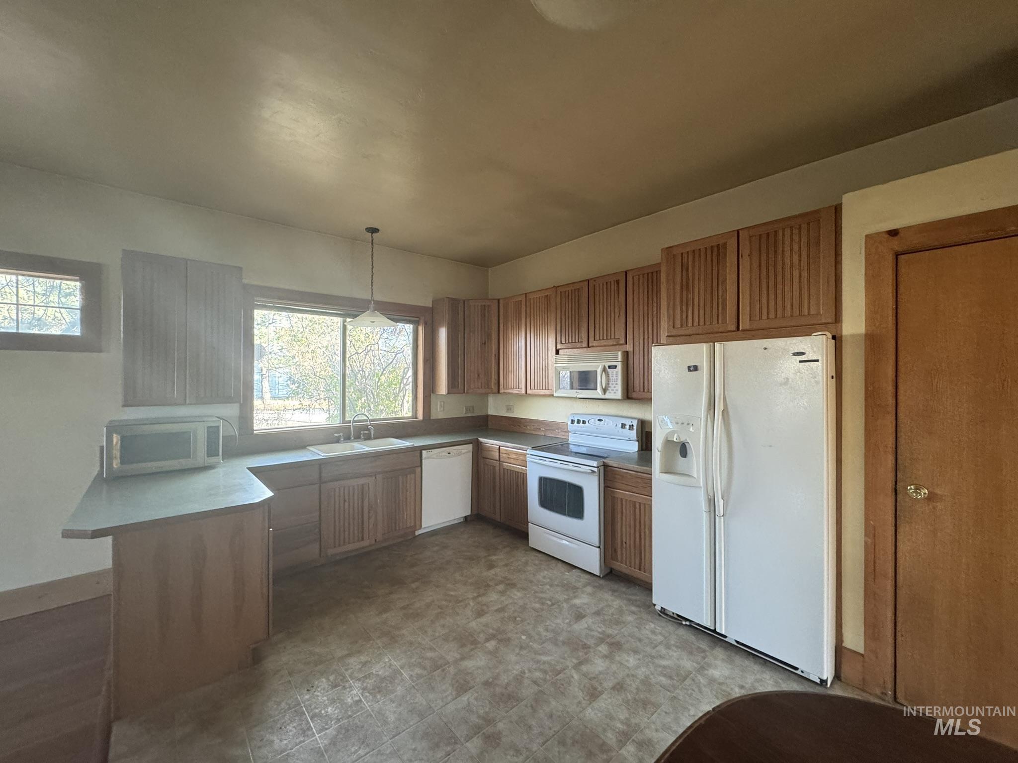 Kitchen with white appliances, a peninsula, decorative light fixtures, brown cabinetry, and light countertops