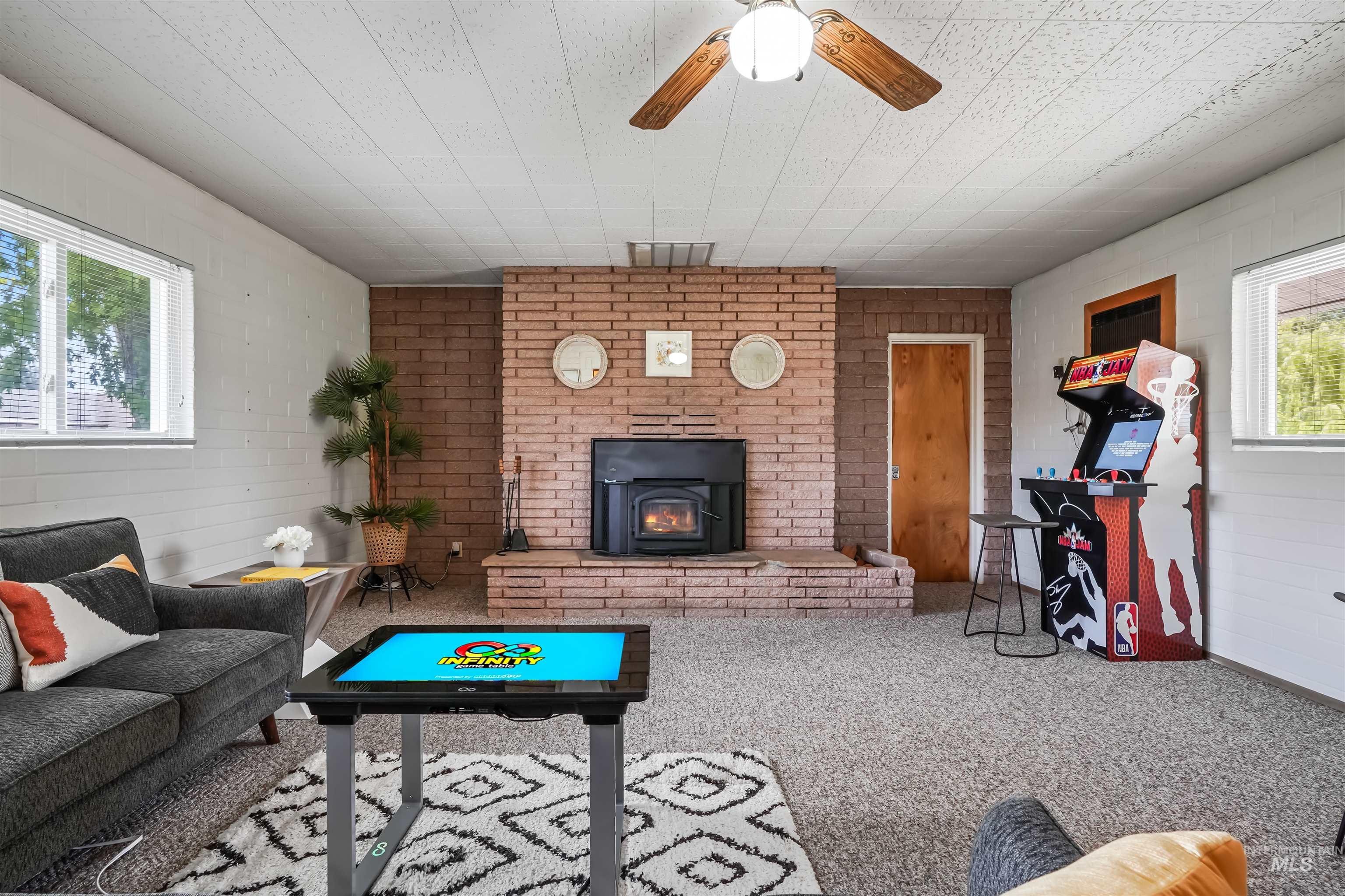 Carpeted living room with a wood stove, brick wall, and wood walls