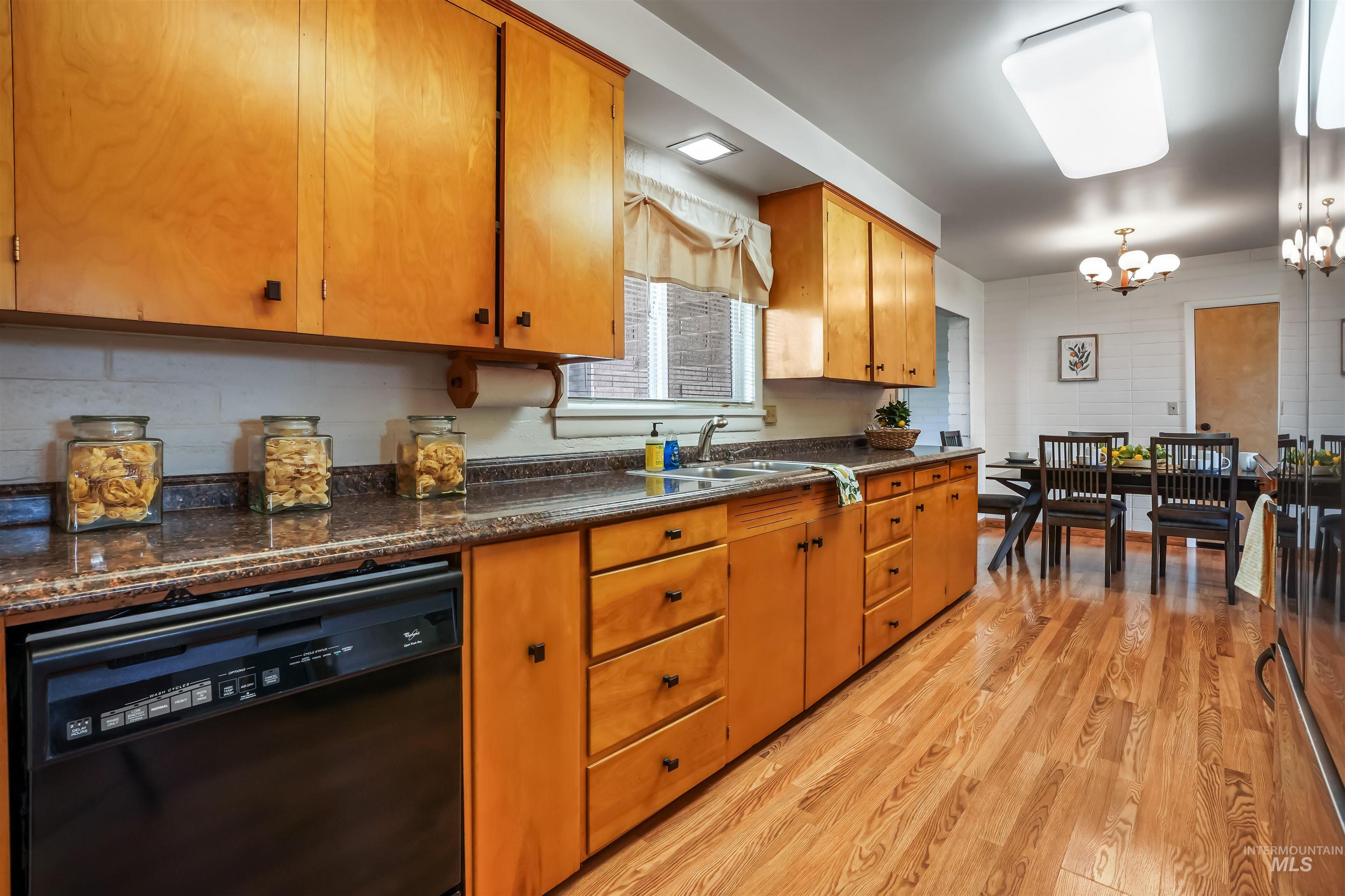 Kitchen with dishwasher, brown cabinetry, light wood-style floors, and a chandelier