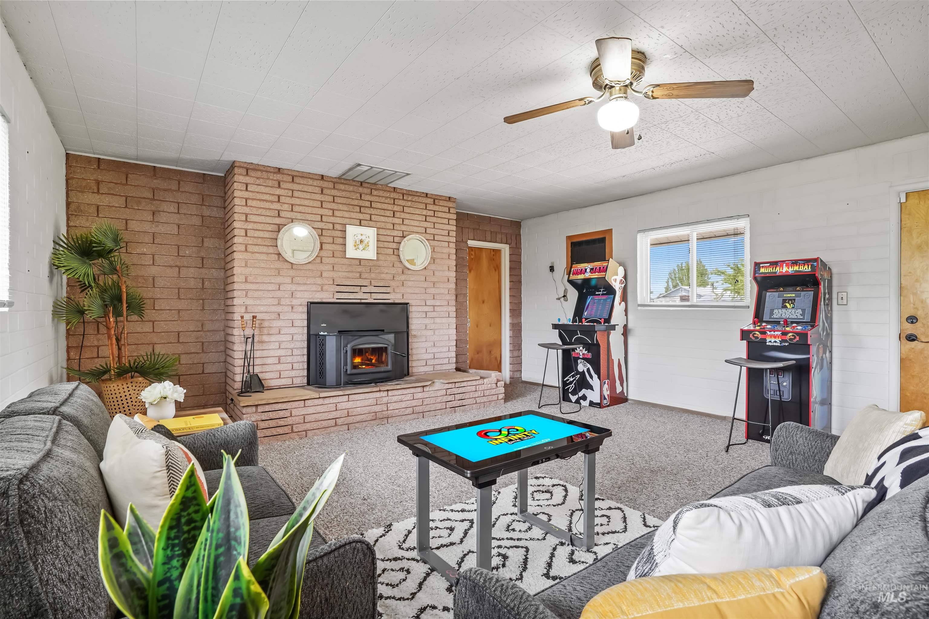 Carpeted living area with brick wall, a ceiling fan, and a wood stove