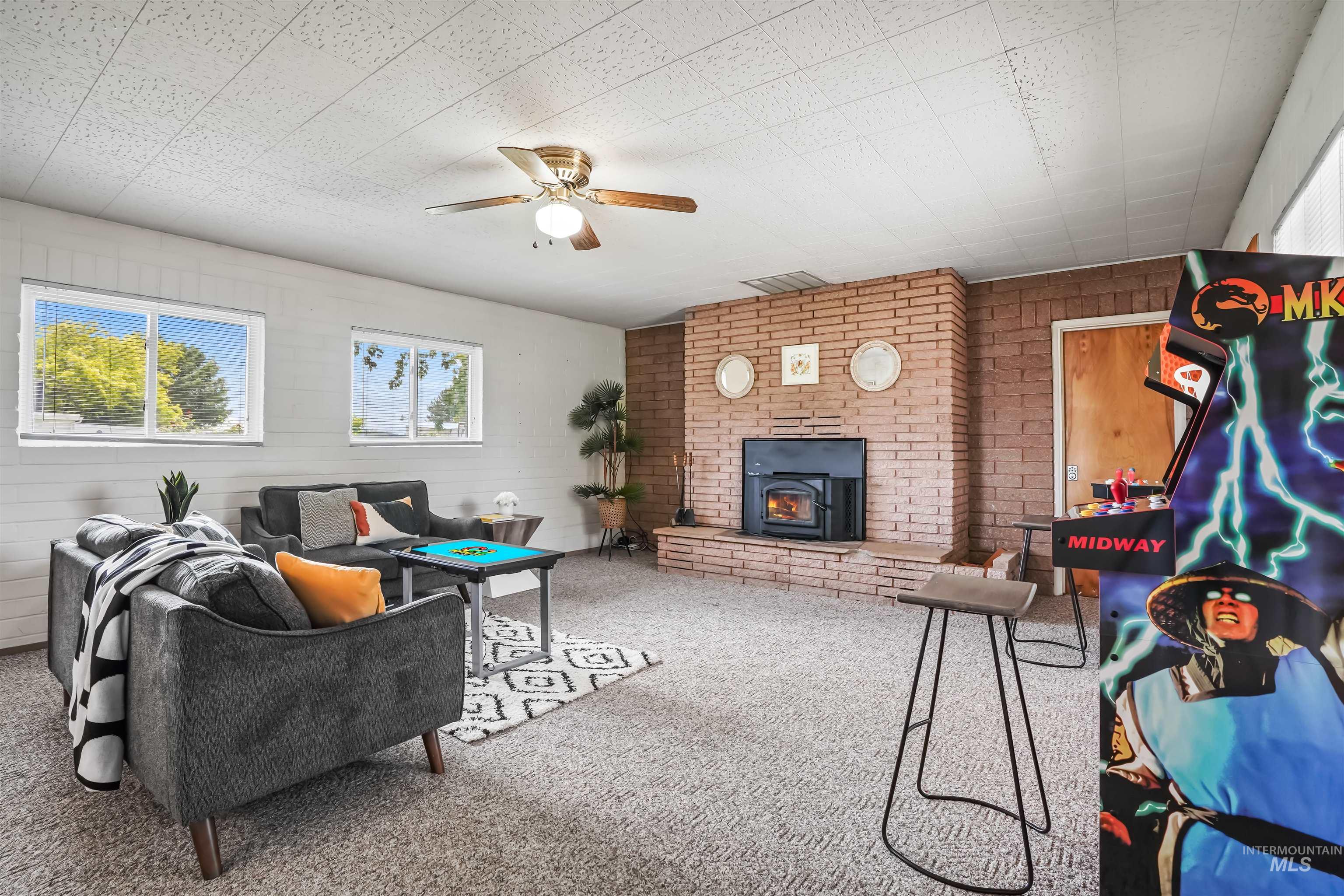 Carpeted living area with a wood stove, a ceiling fan, and wooden walls