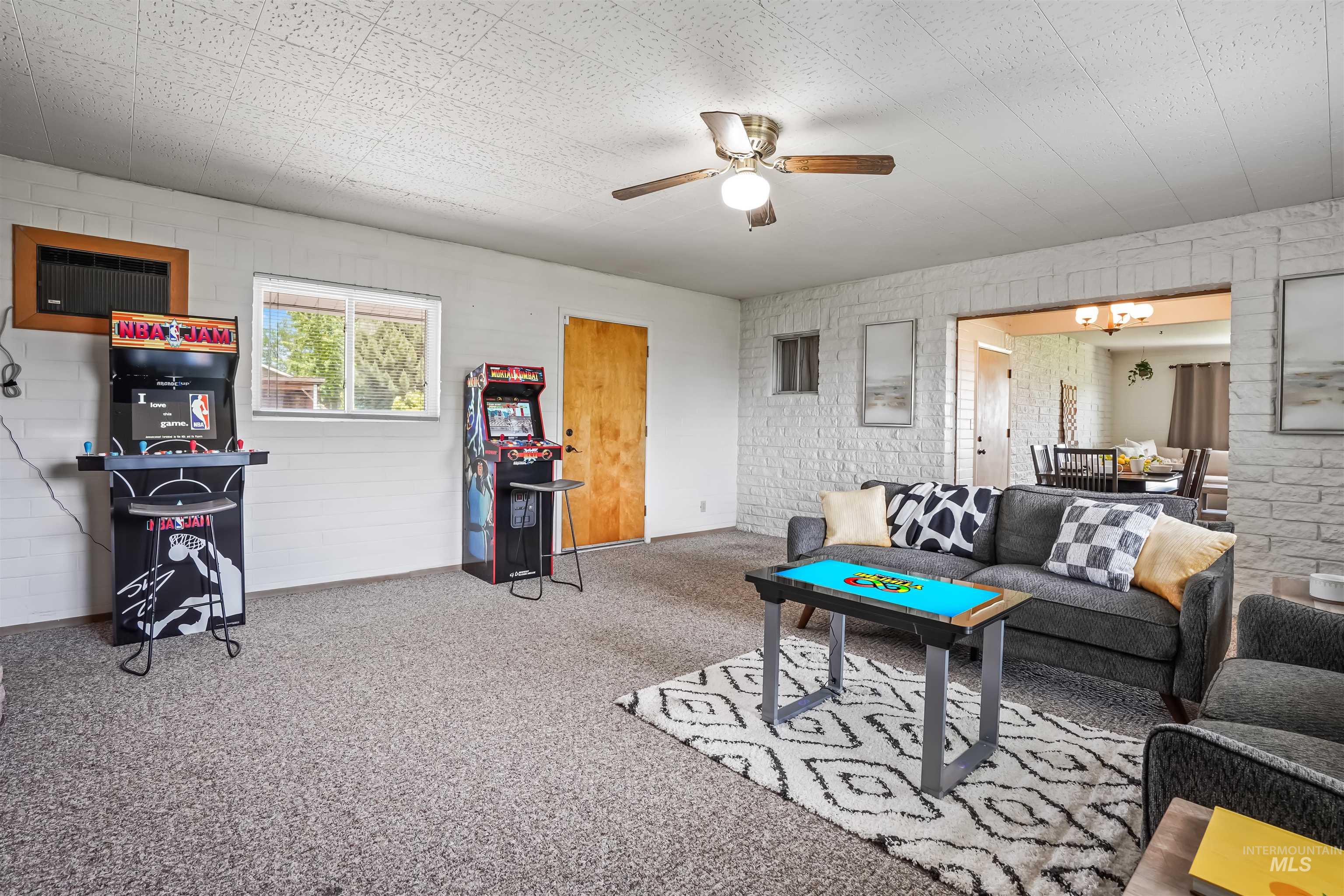 Living area featuring carpet flooring, ceiling fan, a wall unit AC, and brick wall