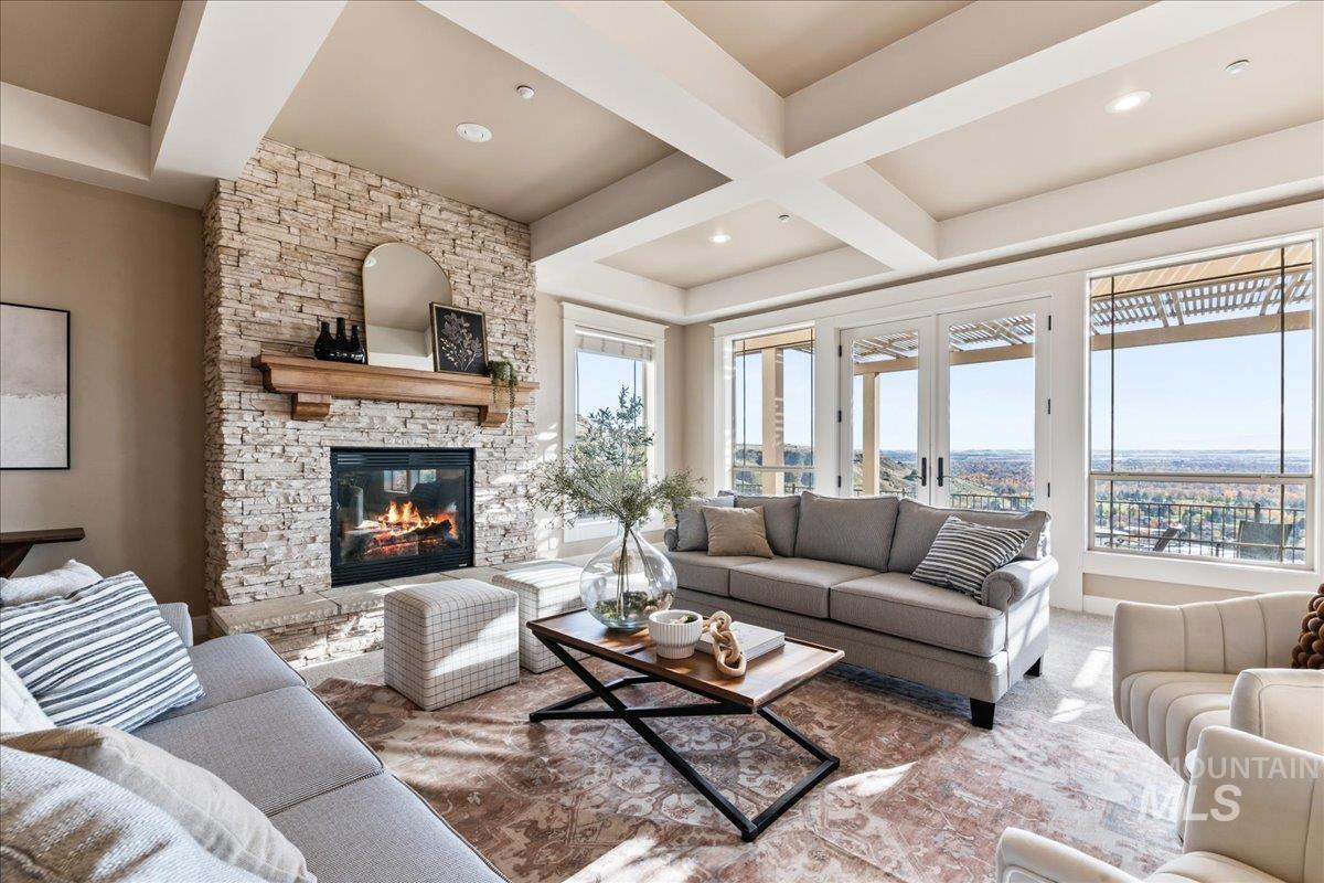 Living area featuring beam ceiling, a stone fireplace, coffered ceiling, and carpet flooring