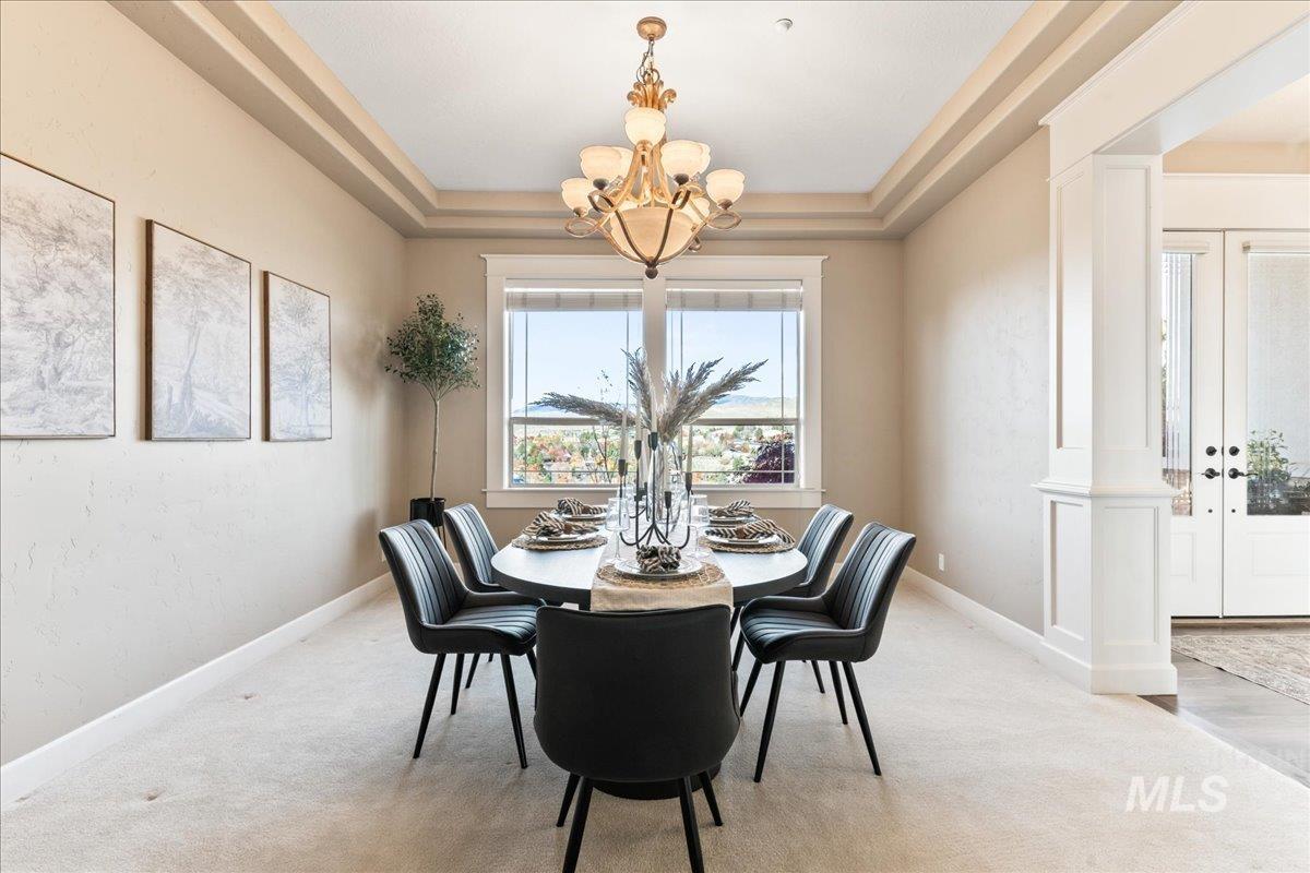 Dining room with a tray ceiling, ornate columns, light colored carpet, and a chandelier