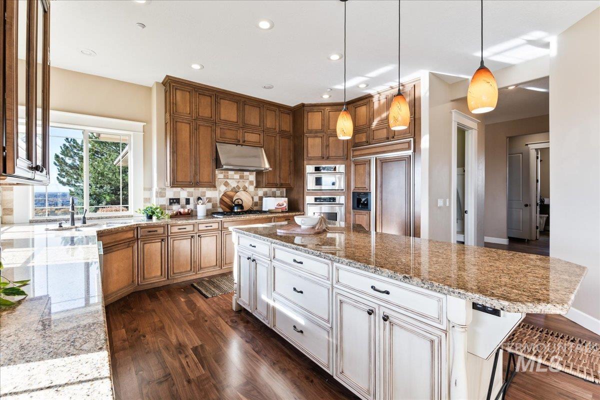Kitchen with dark wood-style flooring, hanging light fixtures, light stone countertops, decorative backsplash, and recessed lighting