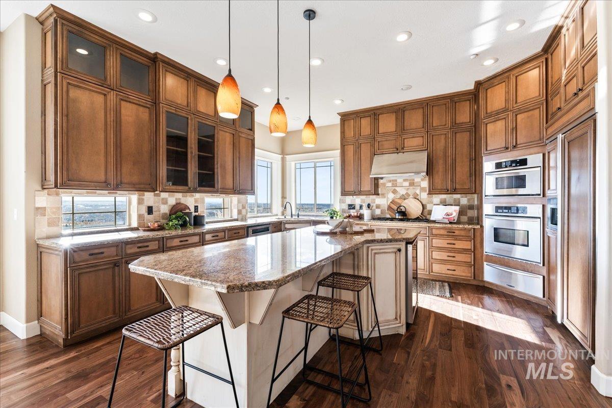 Kitchen with a kitchen island, a kitchen bar, hanging light fixtures, glass insert cabinets, and light stone counters
