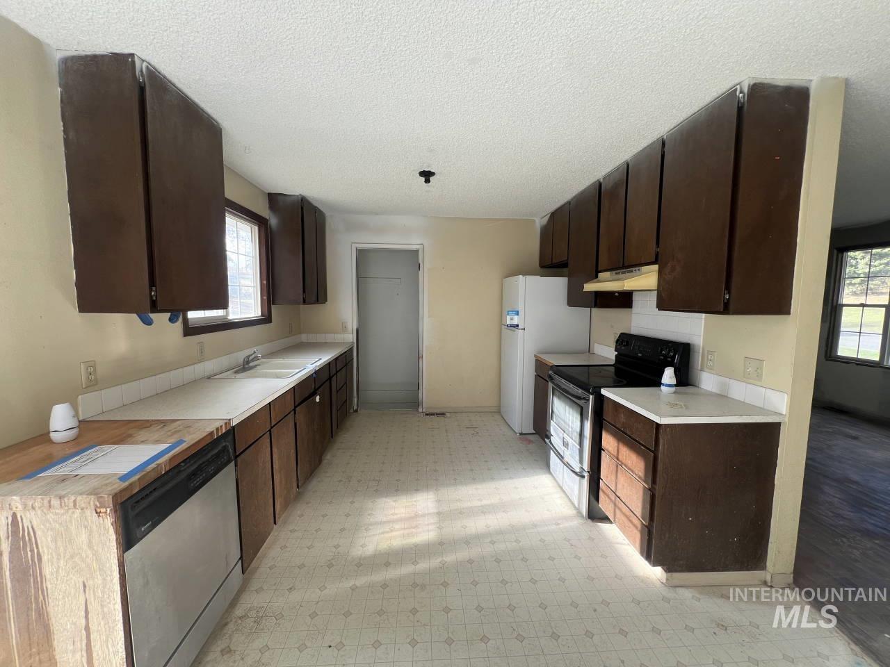 Kitchen with dark brown cabinets, light floors, stainless steel appliances, light countertops, and a textured ceiling