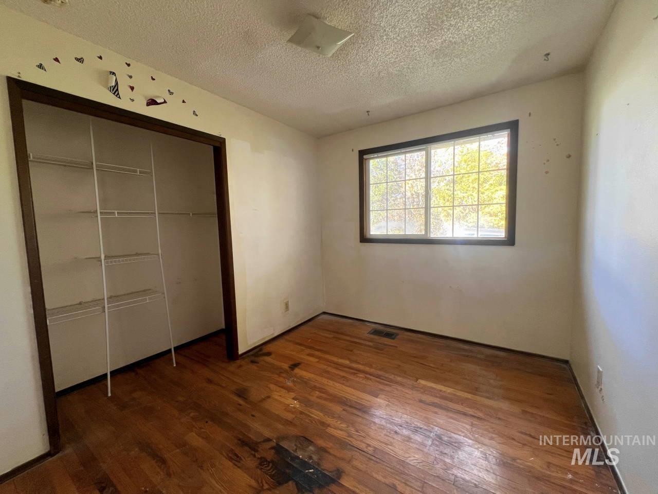 Unfurnished bedroom with dark wood-style flooring, a textured ceiling, and a closet