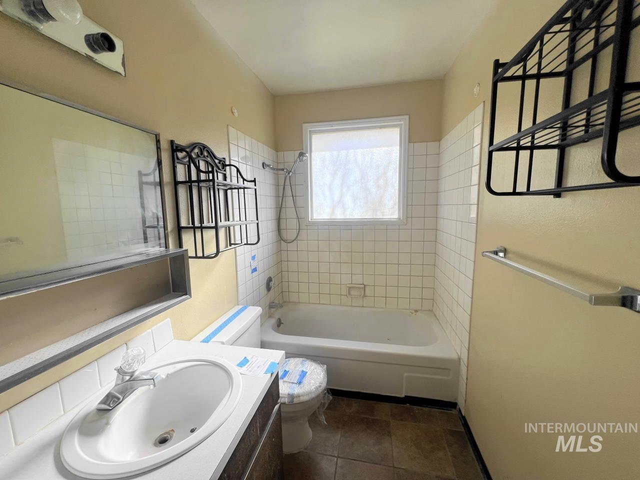 Bathroom featuring washtub / shower combination, vanity, and dark tile patterned floors