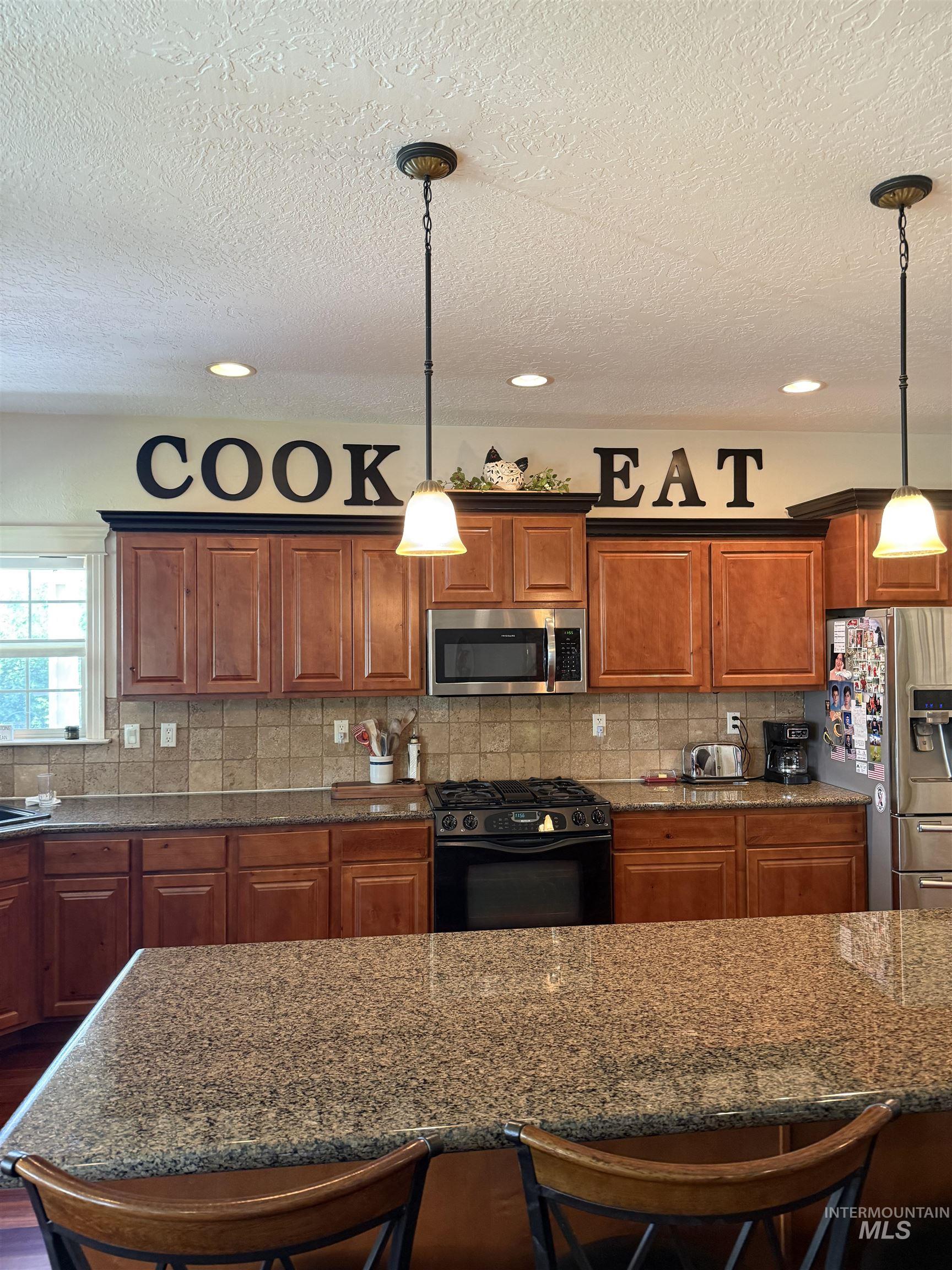 Kitchen featuring a breakfast bar area, appliances with stainless steel finishes, backsplash, a textured ceiling, and recessed lighting