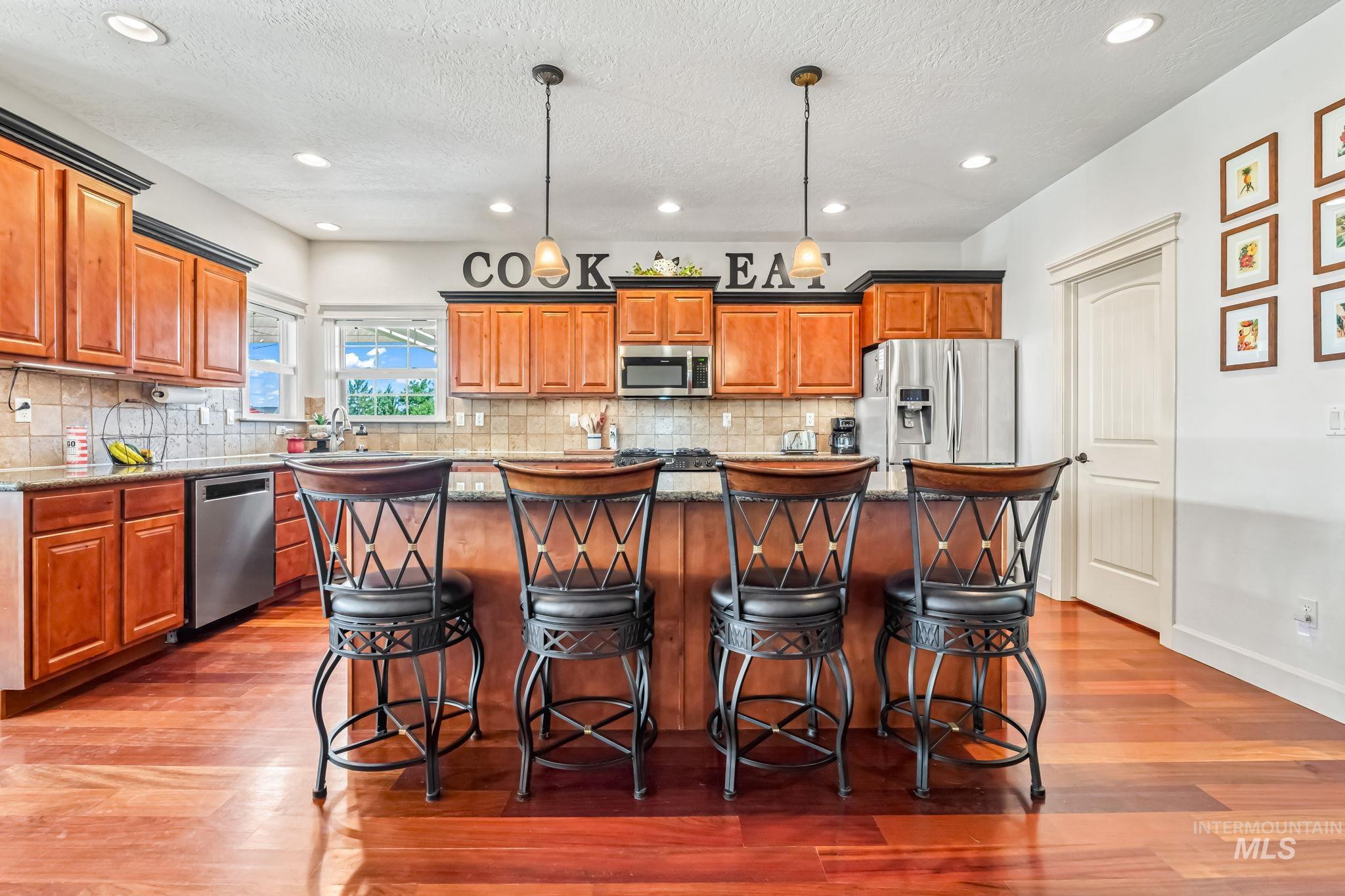 Kitchen with appliances with stainless steel finishes, dark wood-style floors, brown cabinetry, a breakfast bar area, and a textured ceiling