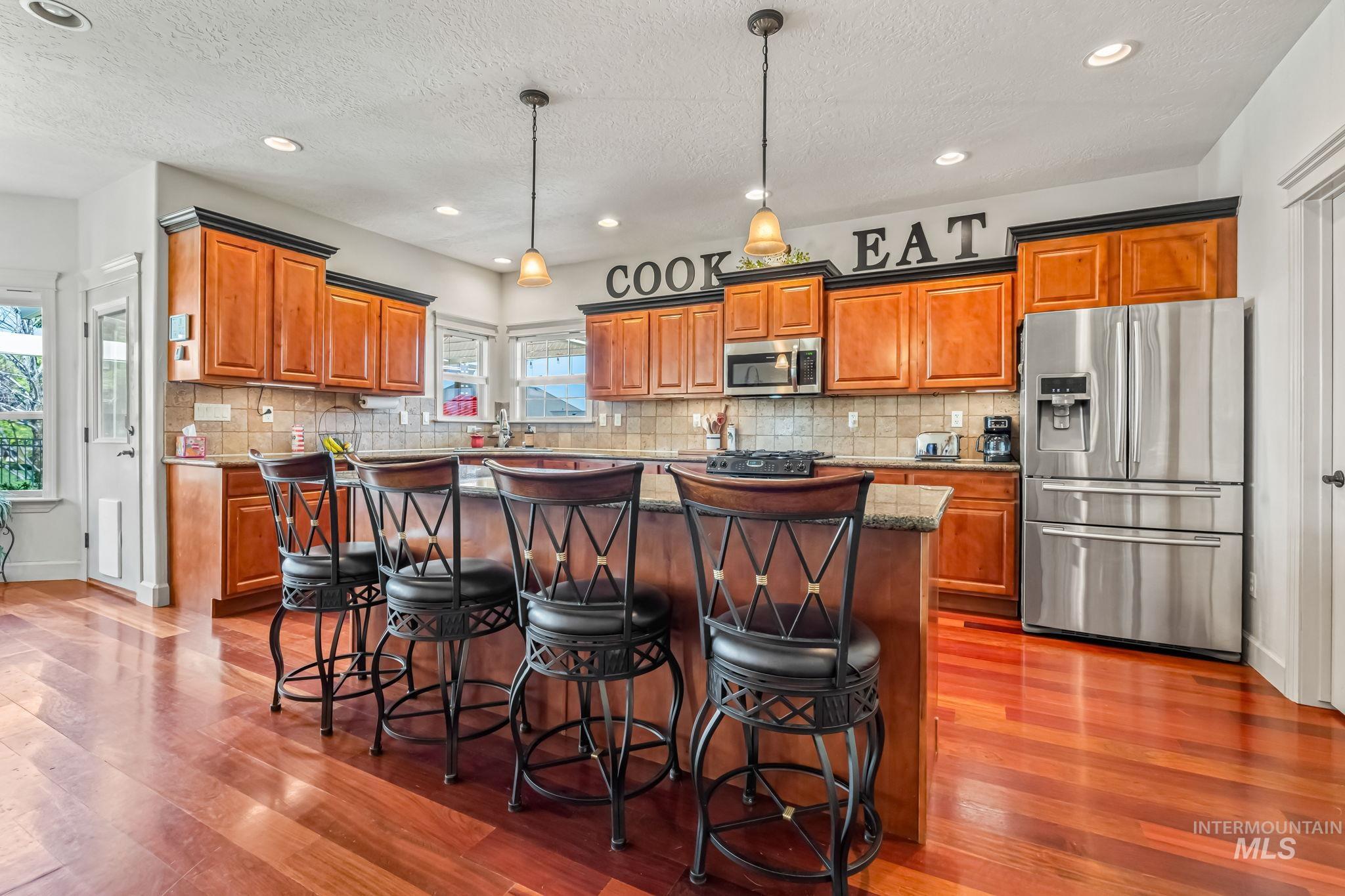 Kitchen with appliances with stainless steel finishes, brown cabinets, a center island, dark wood-style floors, and a textured ceiling