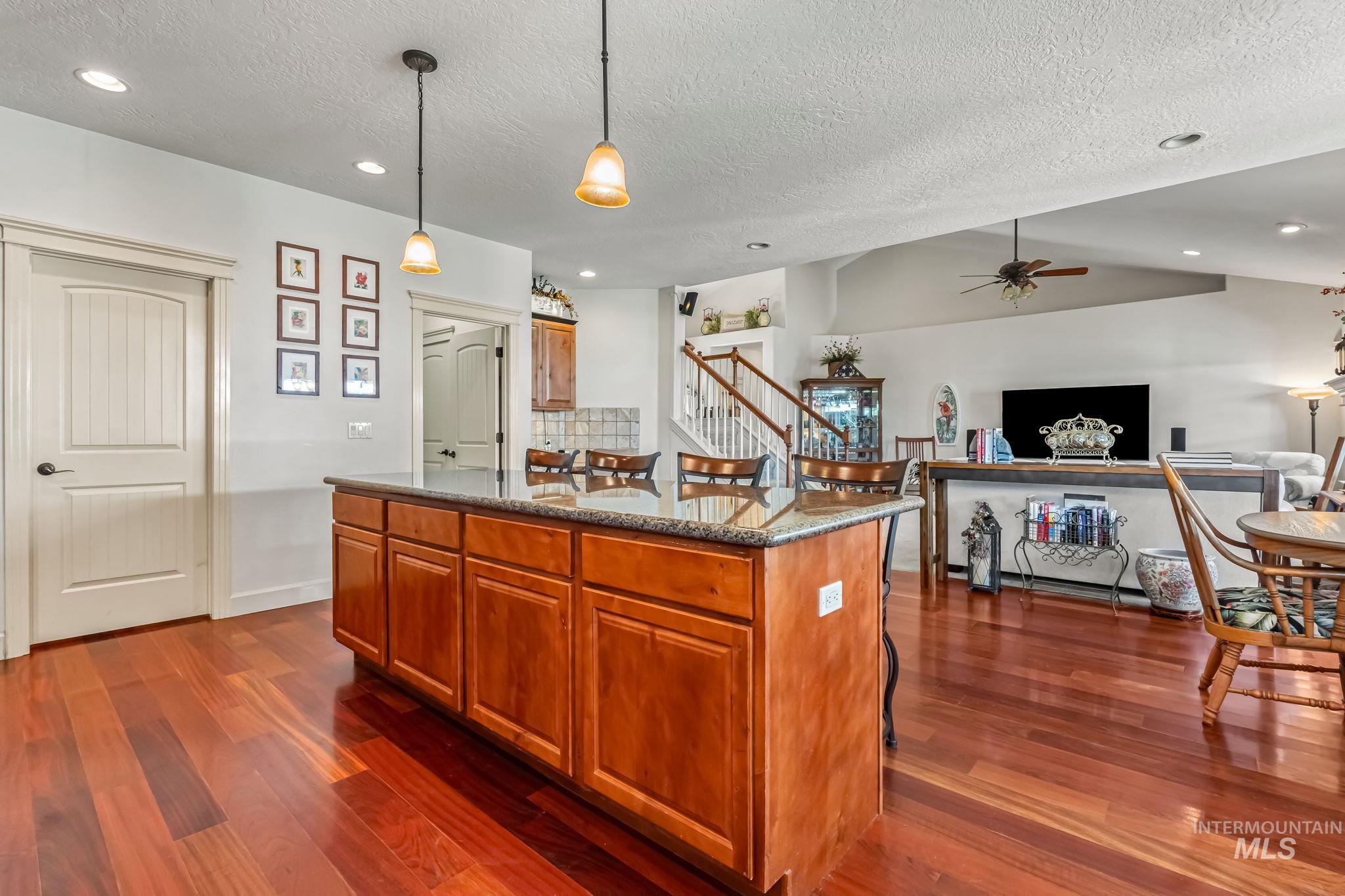 Kitchen with dark wood-style flooring, a textured ceiling, ceiling fan, dark stone countertops, and brown cabinetry