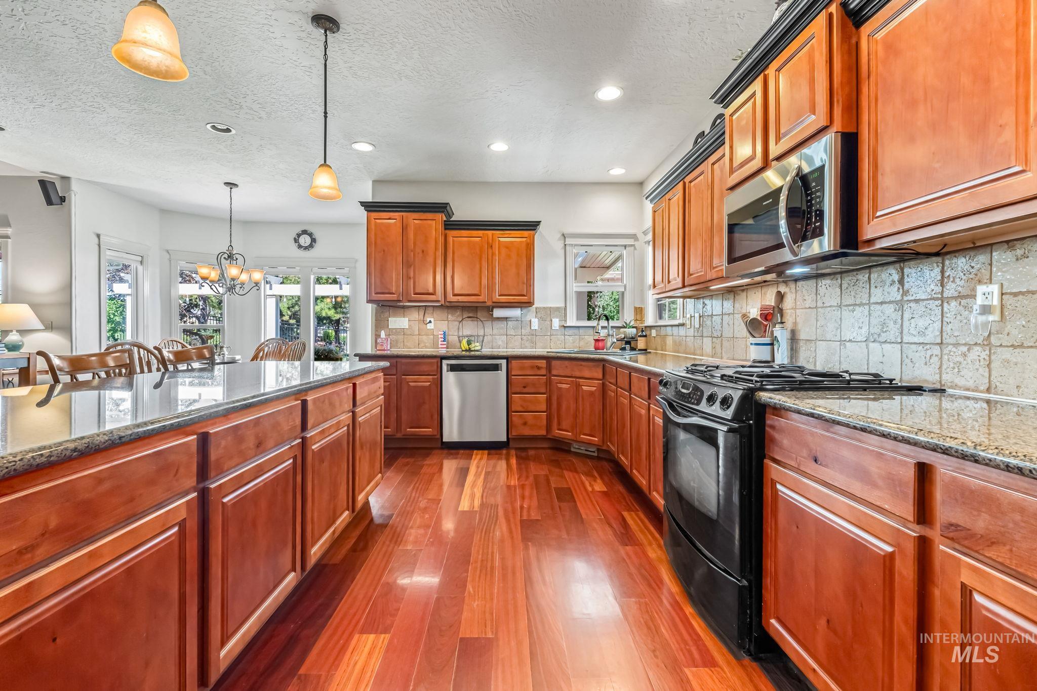 Kitchen featuring stainless steel appliances, dark wood finished floors, a chandelier, stone countertops, and hanging light fixtures