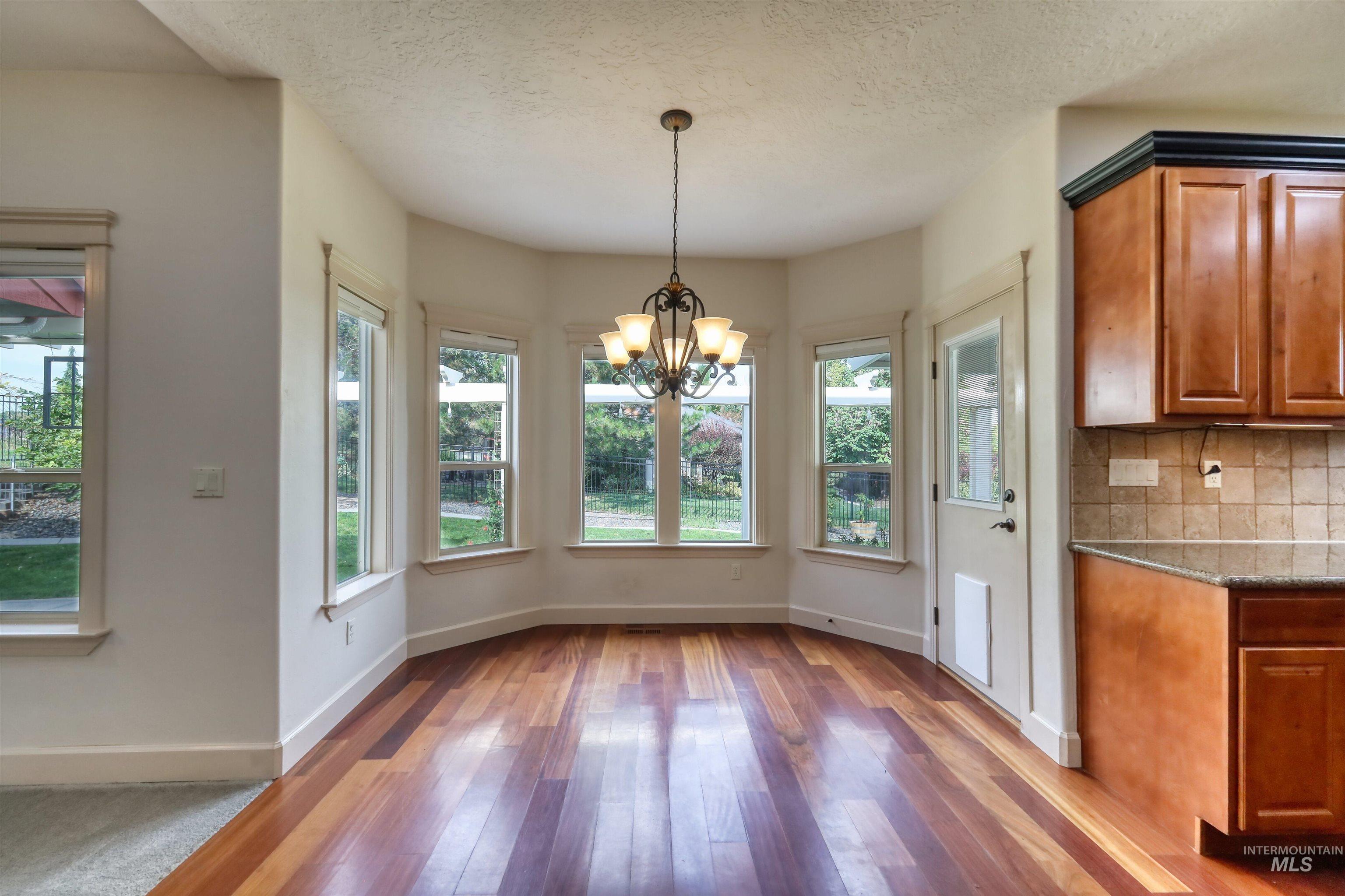 Unfurnished dining area with a chandelier, light wood-type flooring, and a textured ceiling