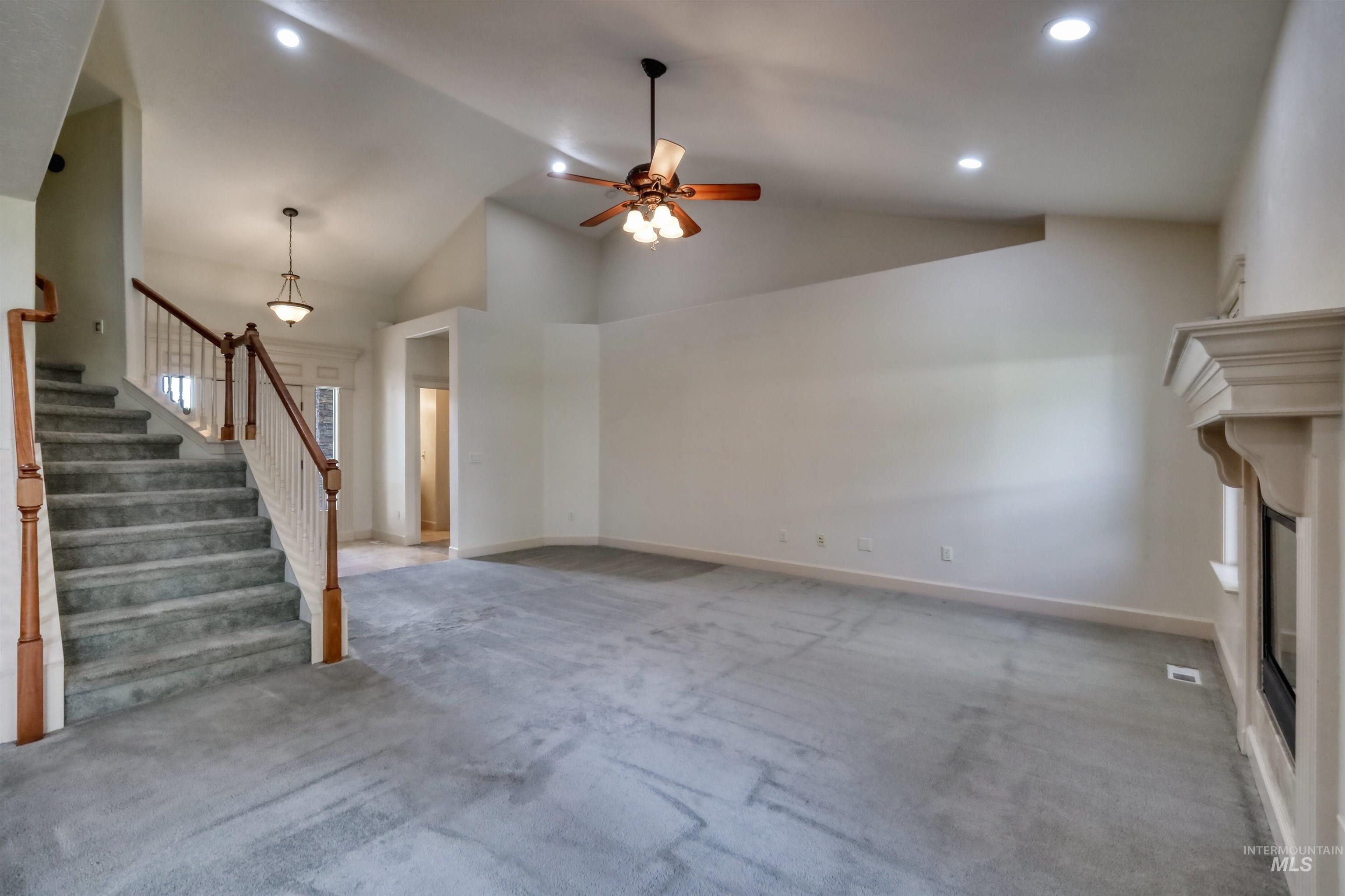Unfurnished living room featuring carpet flooring, ceiling fan, stairway, a glass covered fireplace, and high vaulted ceiling