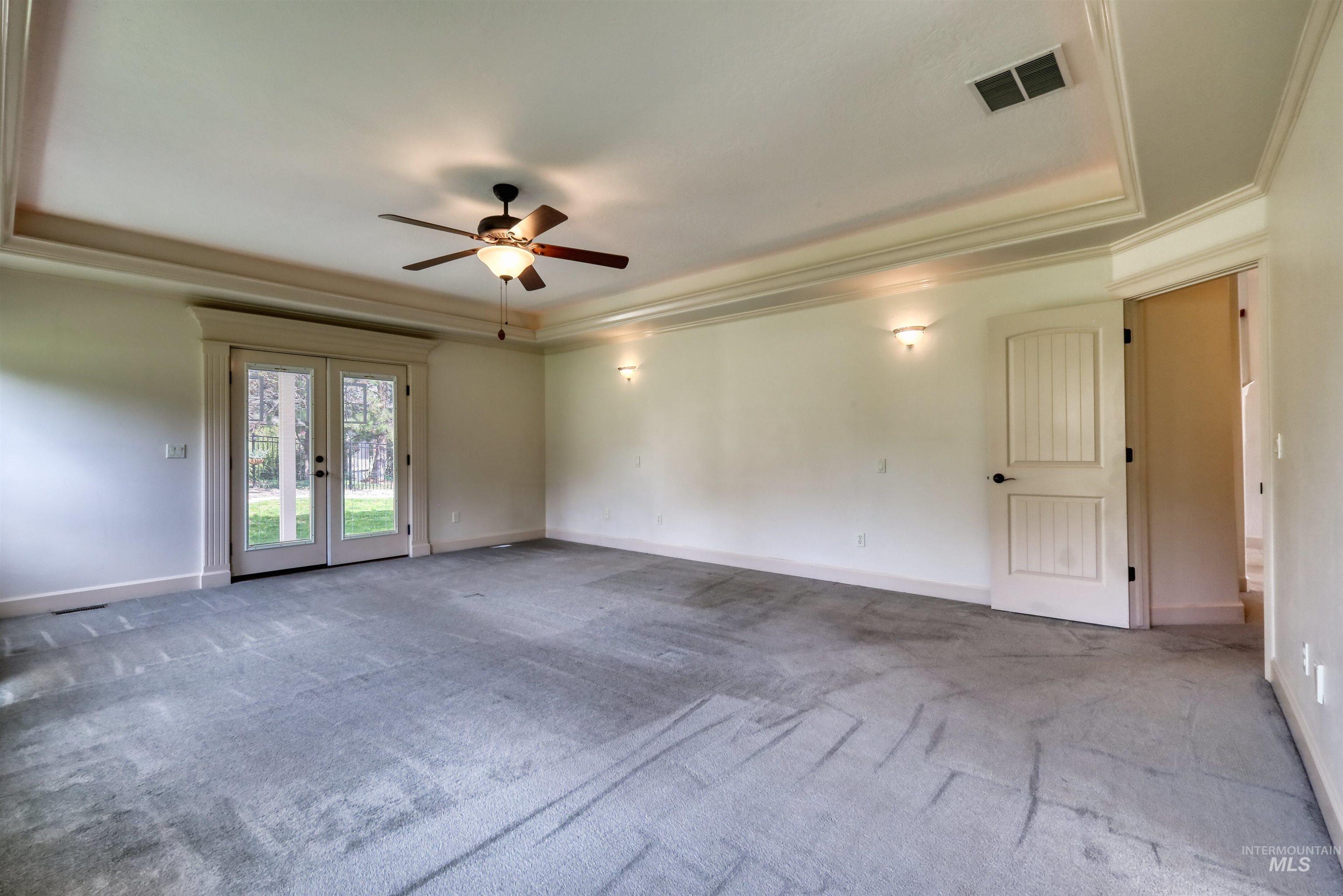Carpeted empty room featuring a tray ceiling, french doors, ornamental molding, and ceiling fan