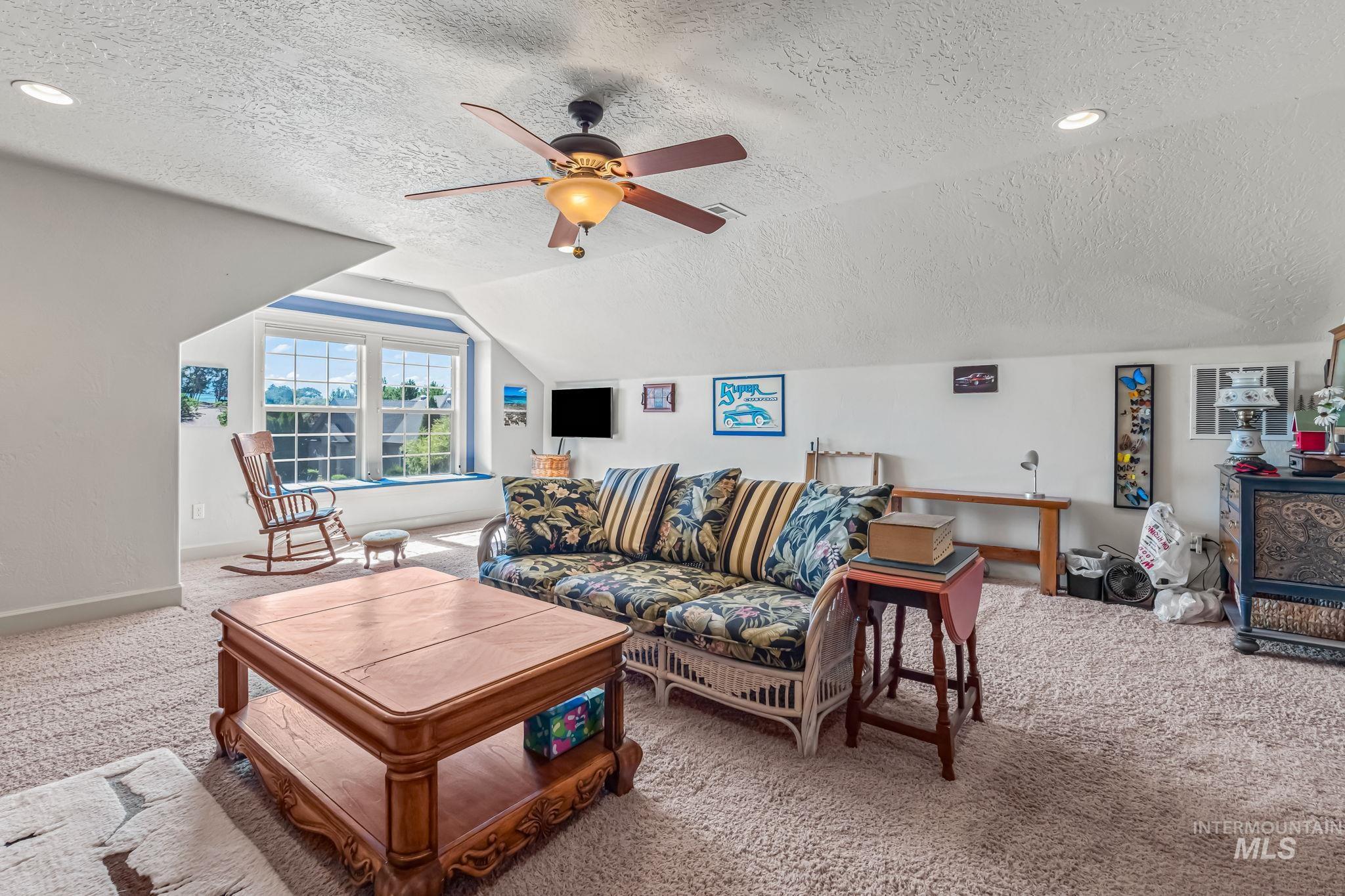 Living area featuring a textured ceiling, carpet, lofted ceiling, and ceiling fan
